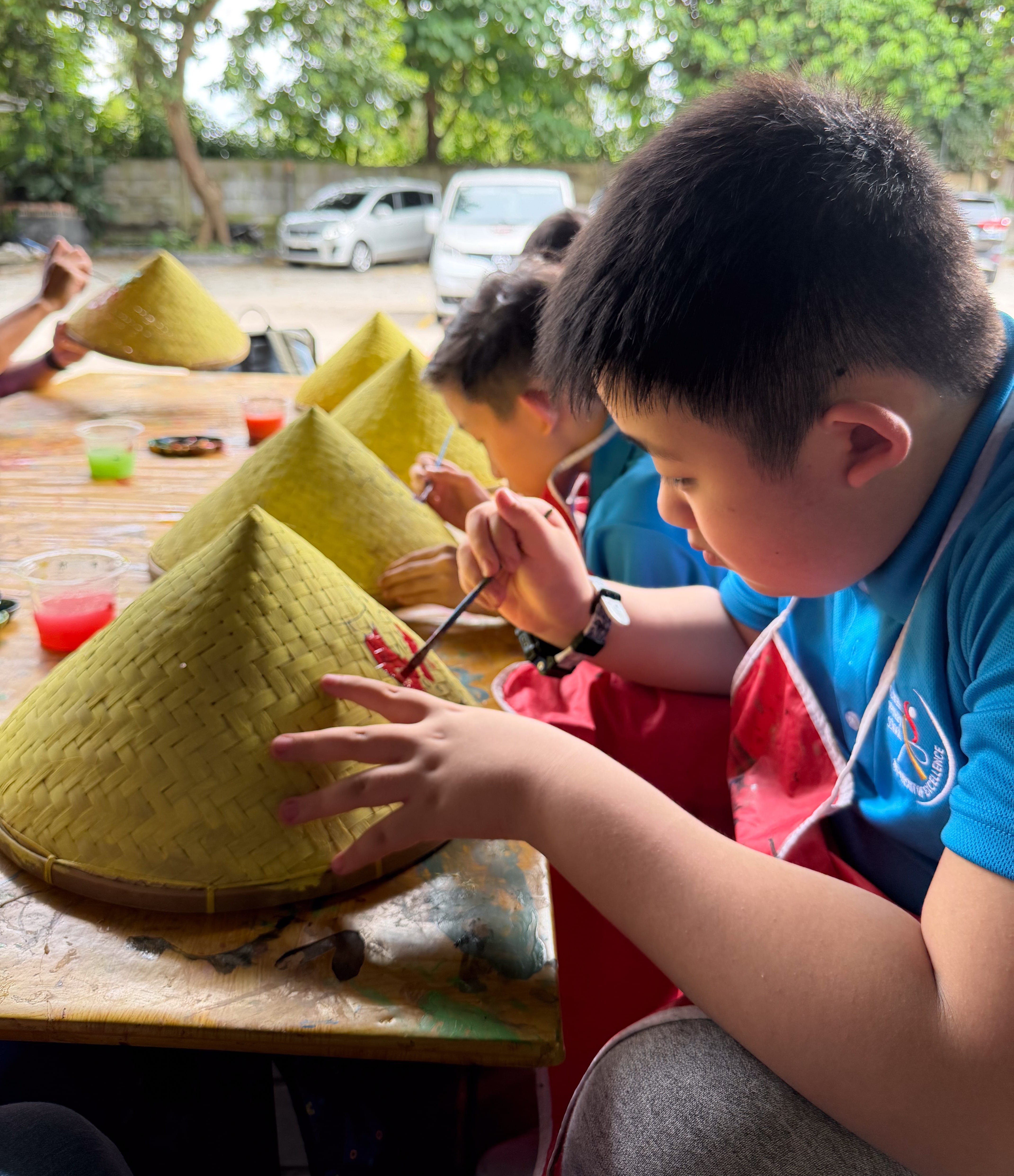 Students painting traditional caping hats during a cultural activity at Godong Ijo