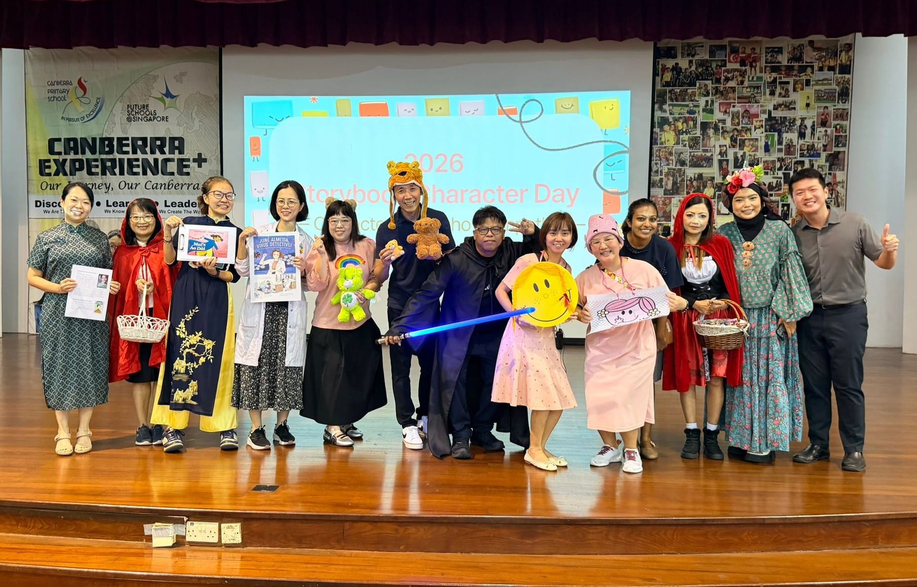 Staff members in storybook character costumes pose on stage before a '2026 Storybook Character Day' screen.
