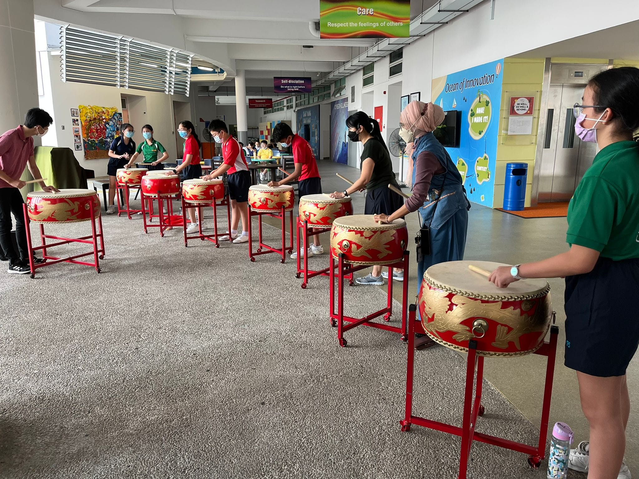 Students and teachers learning to play the Chinese drums together, sharing the joy of learning and creating music.
