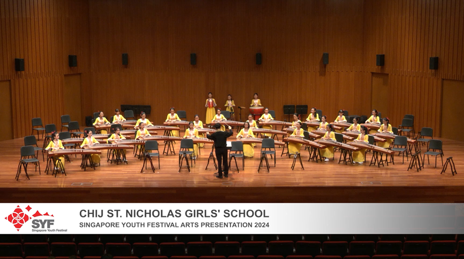 Girls in yellow uniforms play guzheng on a wooden stage, led by a conductor, at SYF Arts Presentation 2022.
