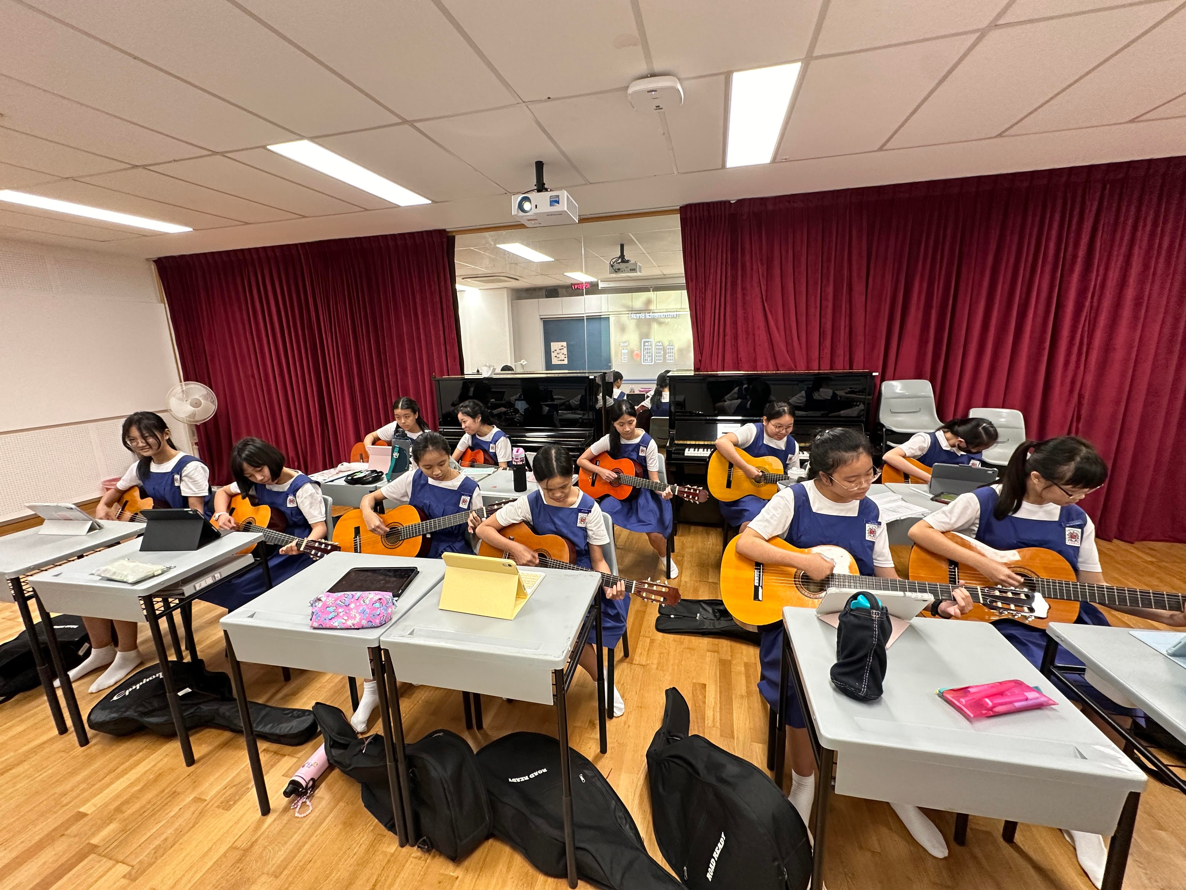 Students learning classical guitar arrangements using tablets in a classroom.