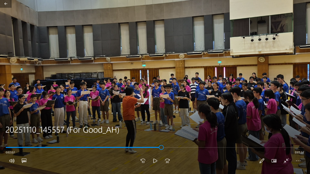 Combined school choir practices enthusiastically inside a spacious auditorium.