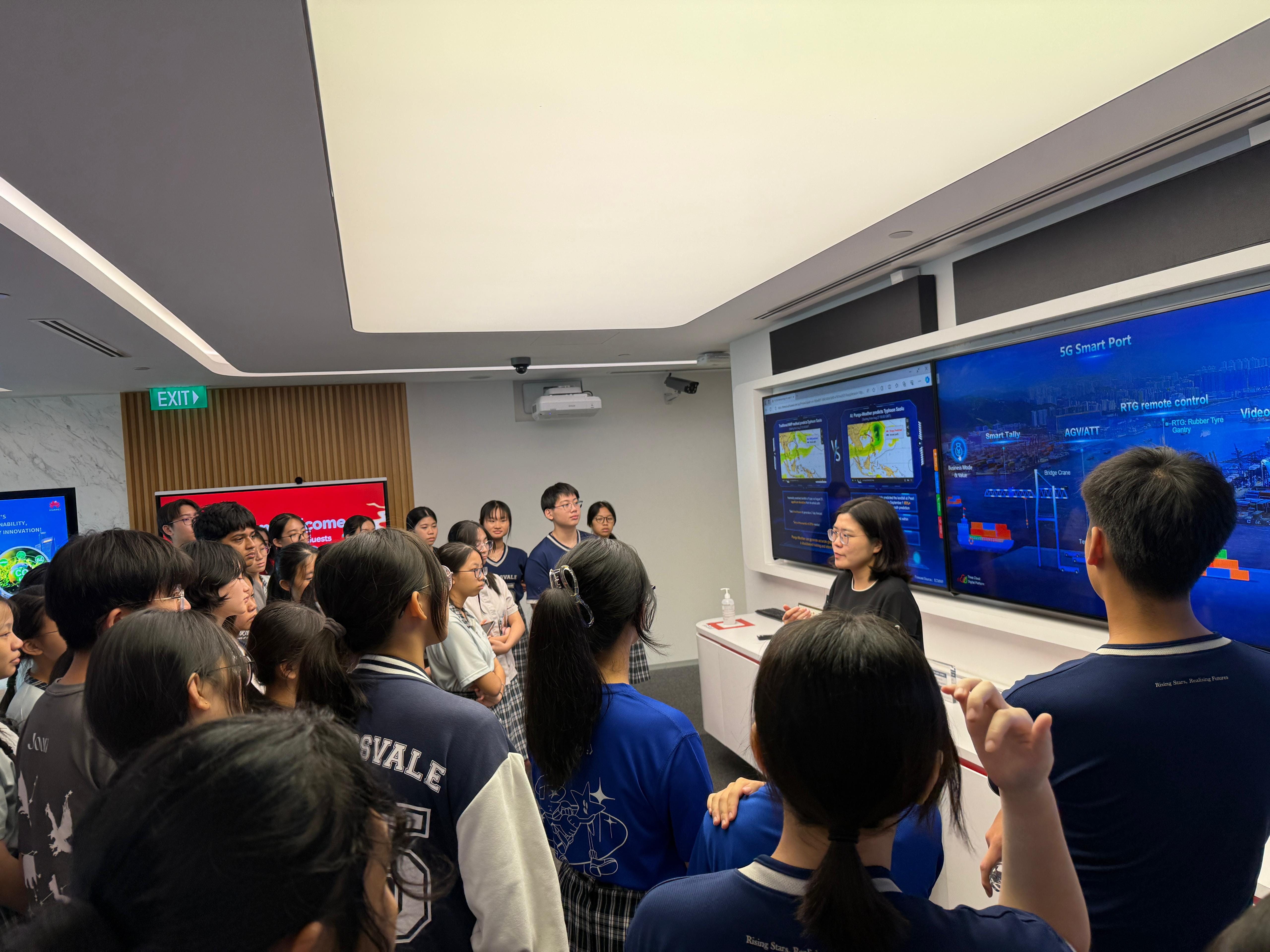 A group of students listens to a presenter in a room with large screens displaying a 5G Smart Port presentation.