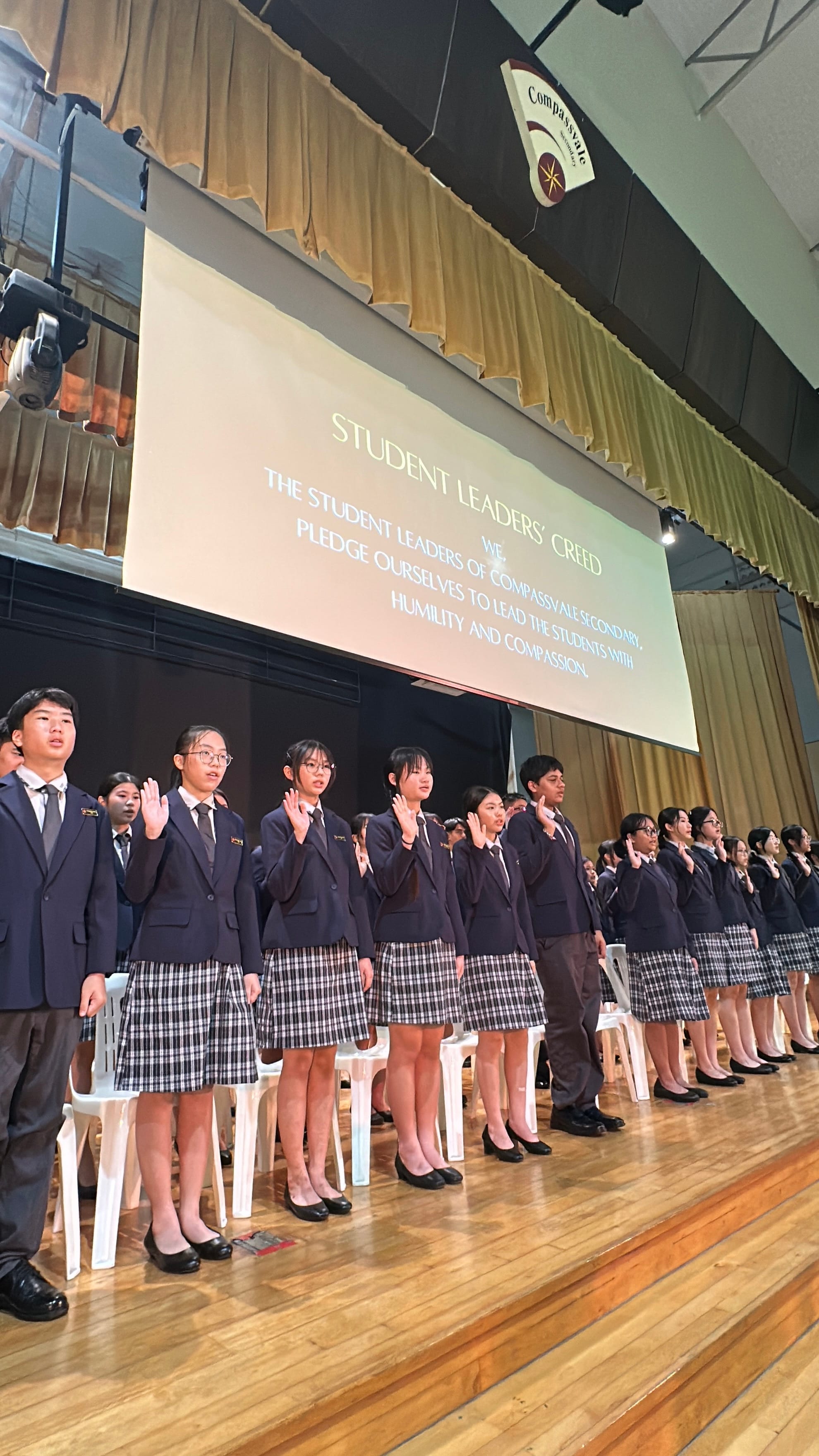 Students in navy blazers raise right hands on a stage reciting the Student Leaders' Creed at Compassvale Secondary.