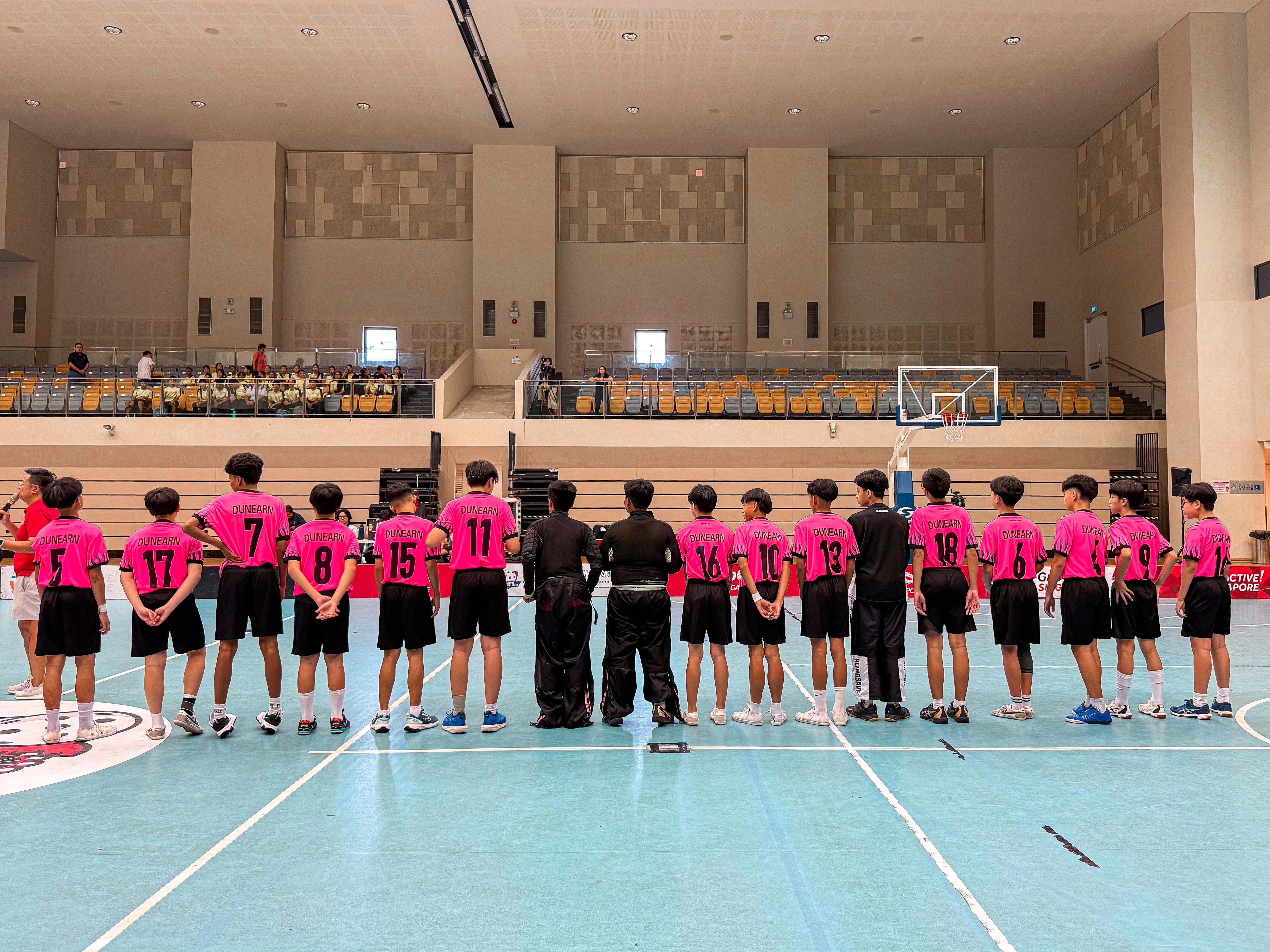 A youth basketball team in pink Dunearn jerseys lines up on an indoor court facing away from the camera.