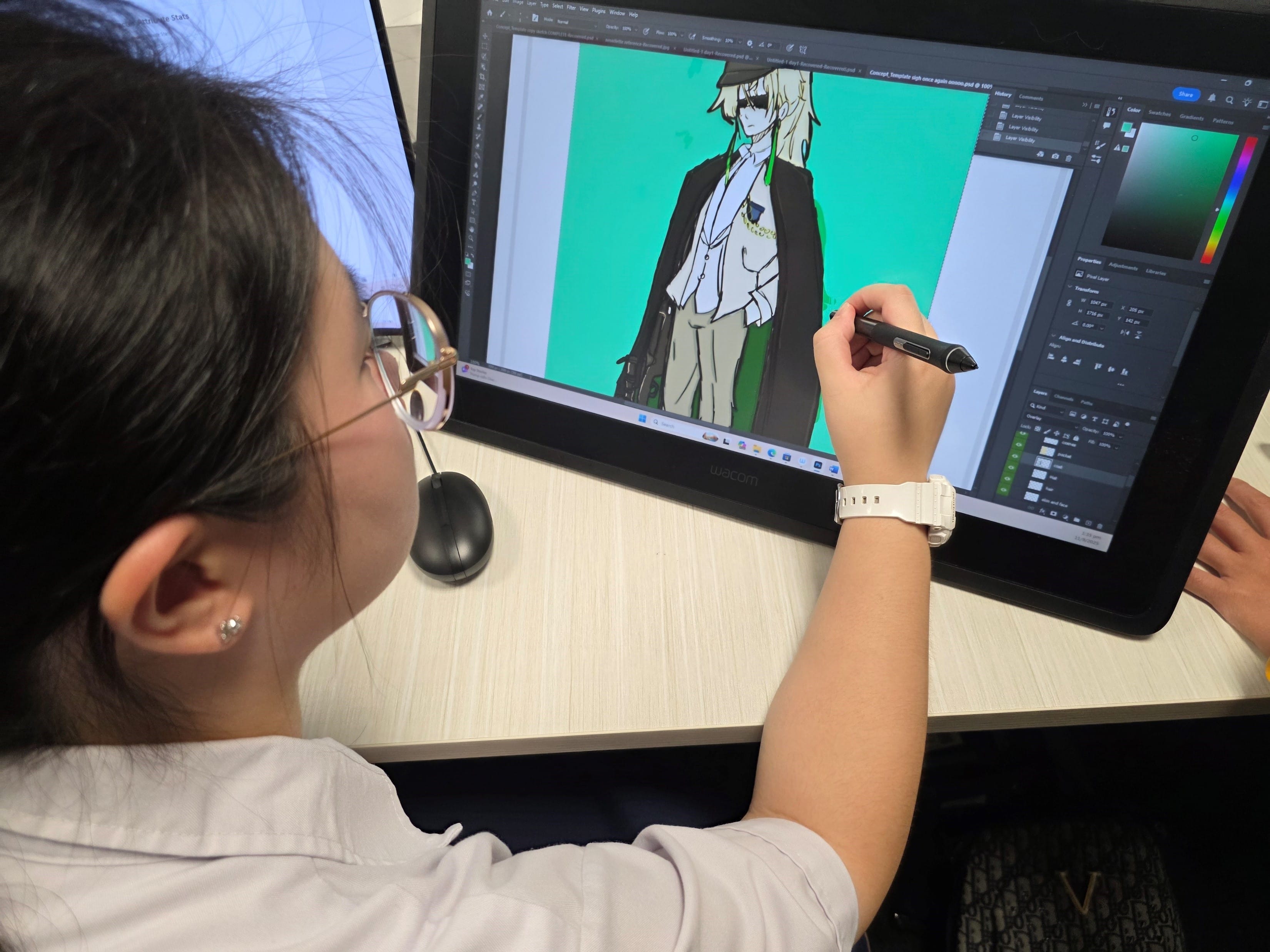 A young woman with glasses draws an anime character in Photoshop on a Wacom pen display using a stylus.