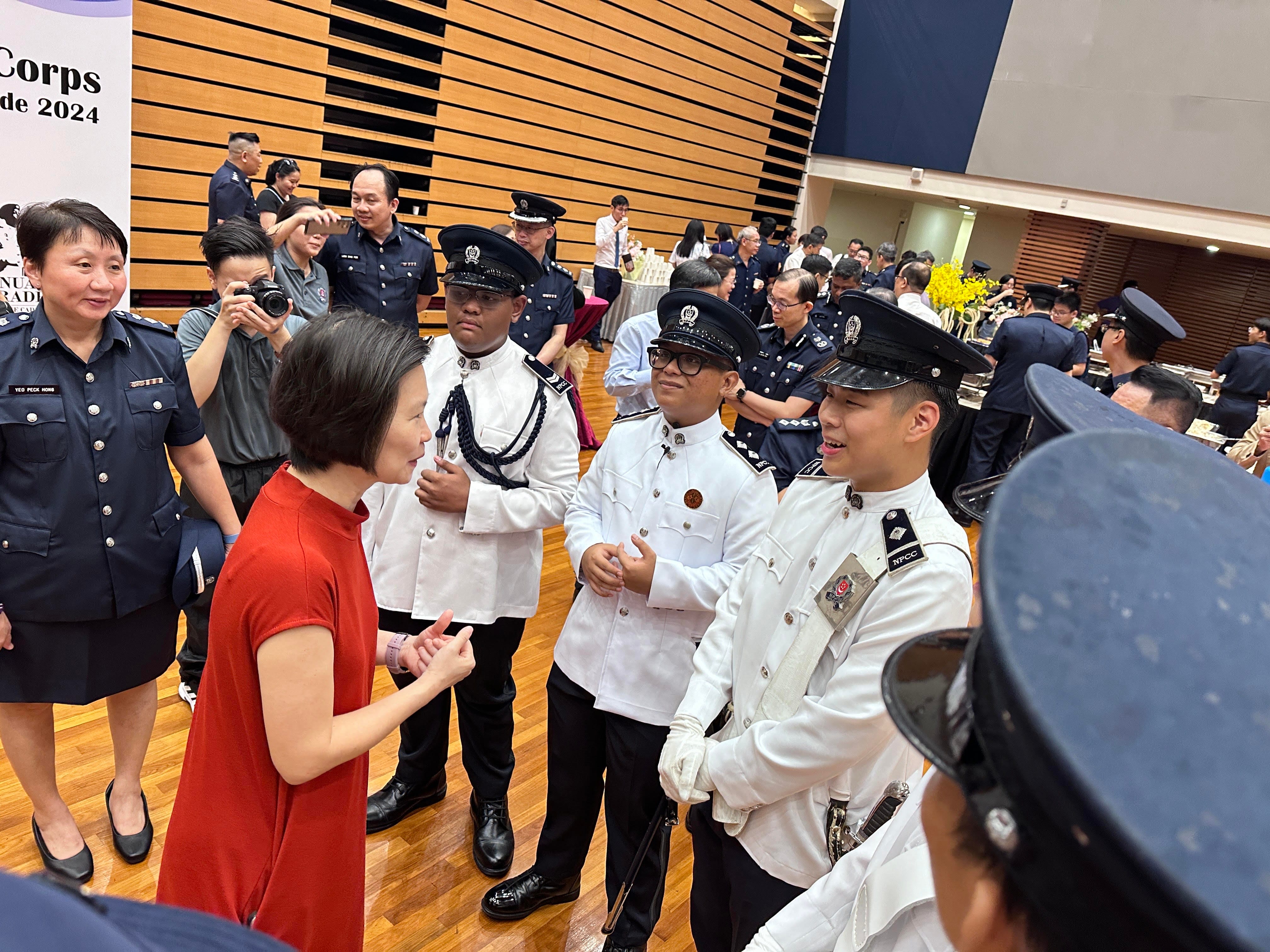 A woman in red speaks with officers in white ceremonial uniforms at a 2024 Corps parade indoor event.