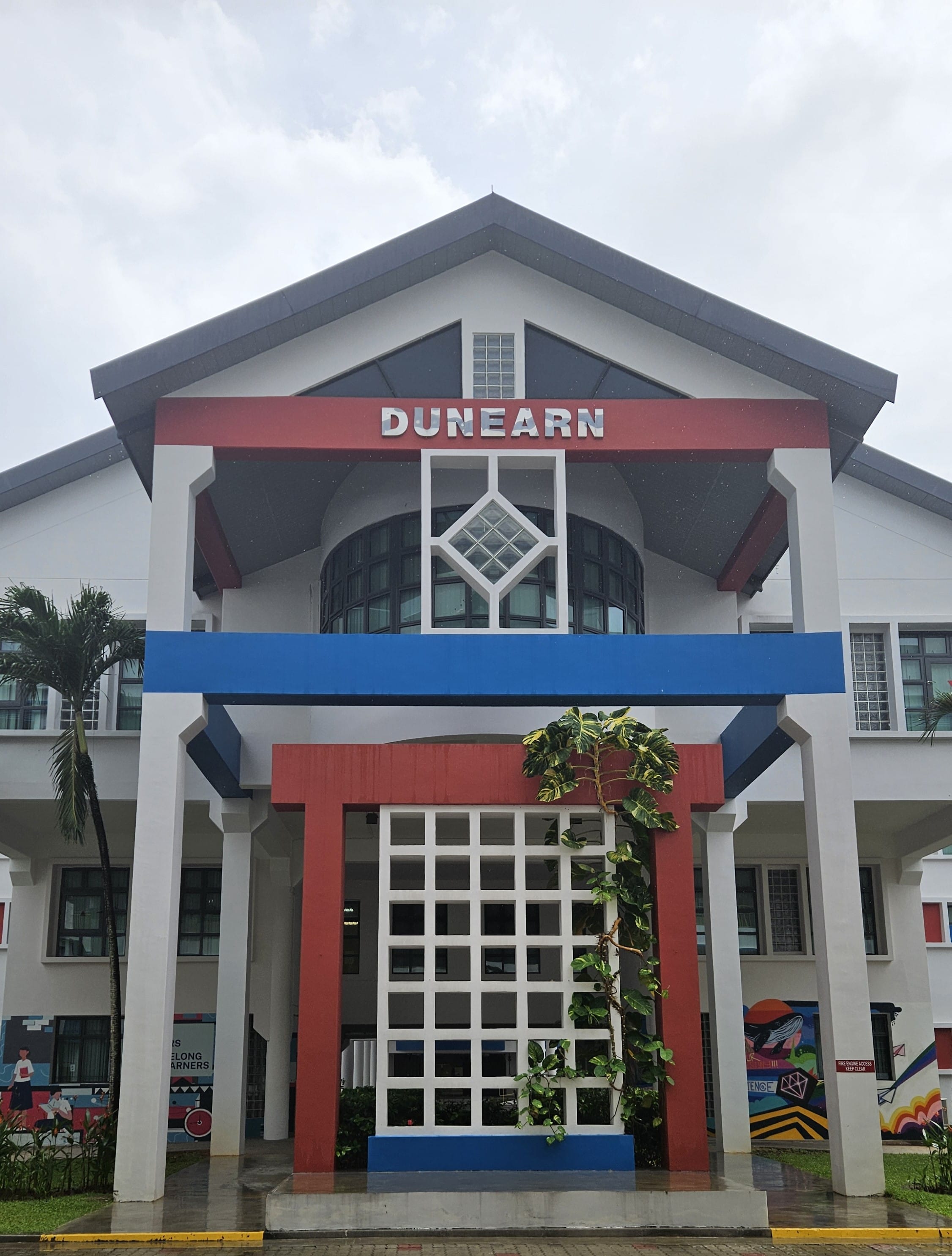 Front entrance of Dunearn building with white facade, red and blue accents, and a grid gate below the sign.