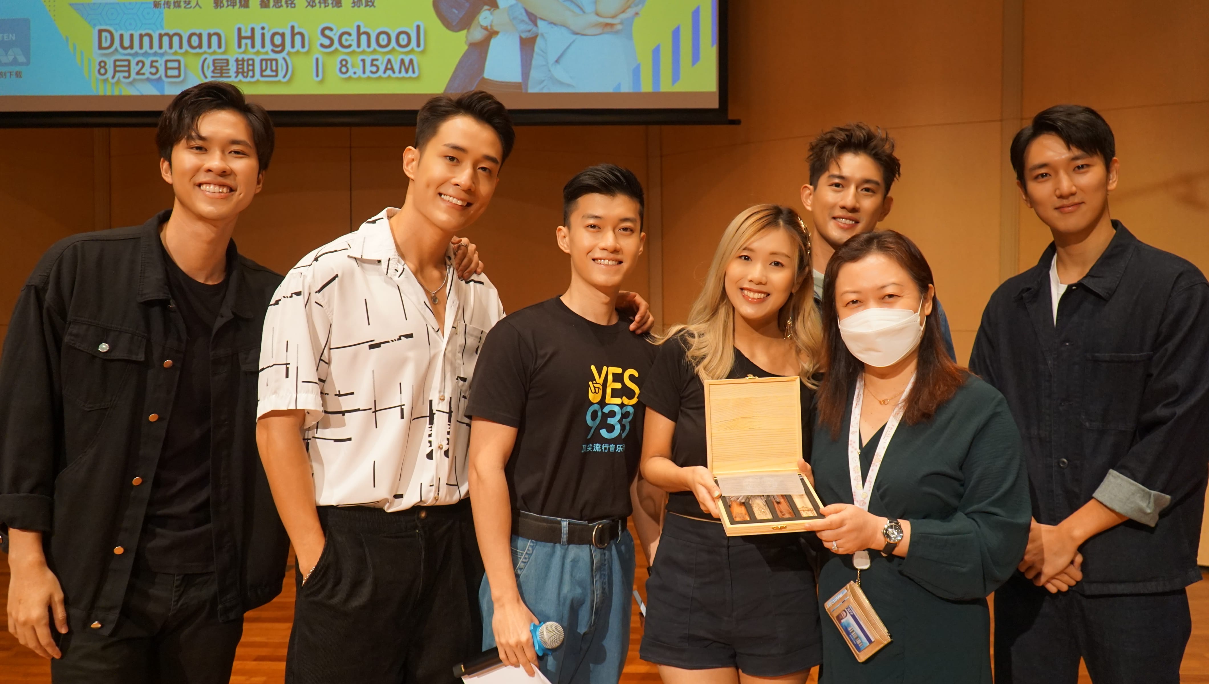 Seven people pose together at a Dunman High School event, with two holding an open wooden gift box.