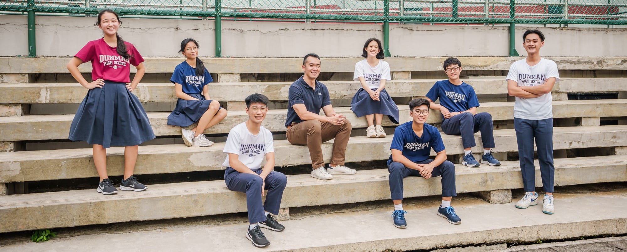 Eight Dunman High School students and a teacher pose on concrete bleachers, smiling at the camera.