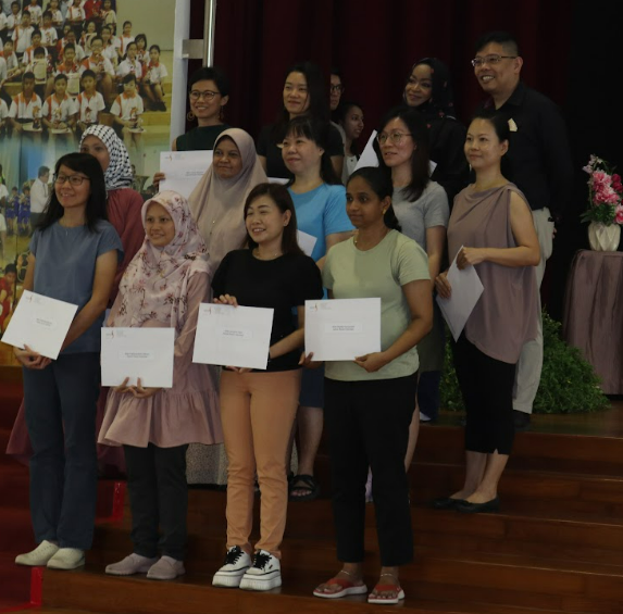 A group of about twelve people posing on a stage, several holding white certificates, at an award ceremony.