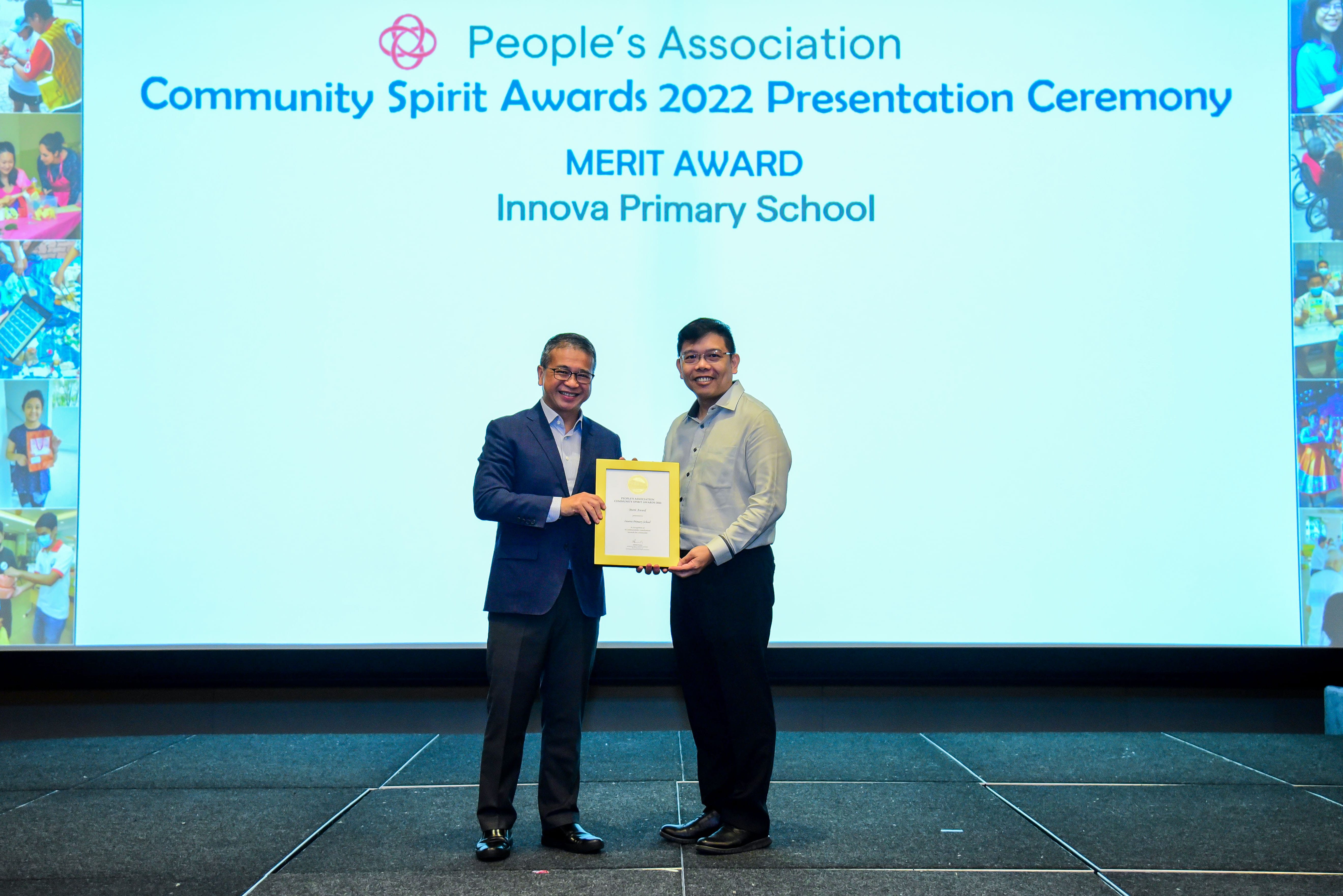 Two men hold a Merit Award certificate on stage at the People's Association Community Spirit Awards 2022 ceremony.