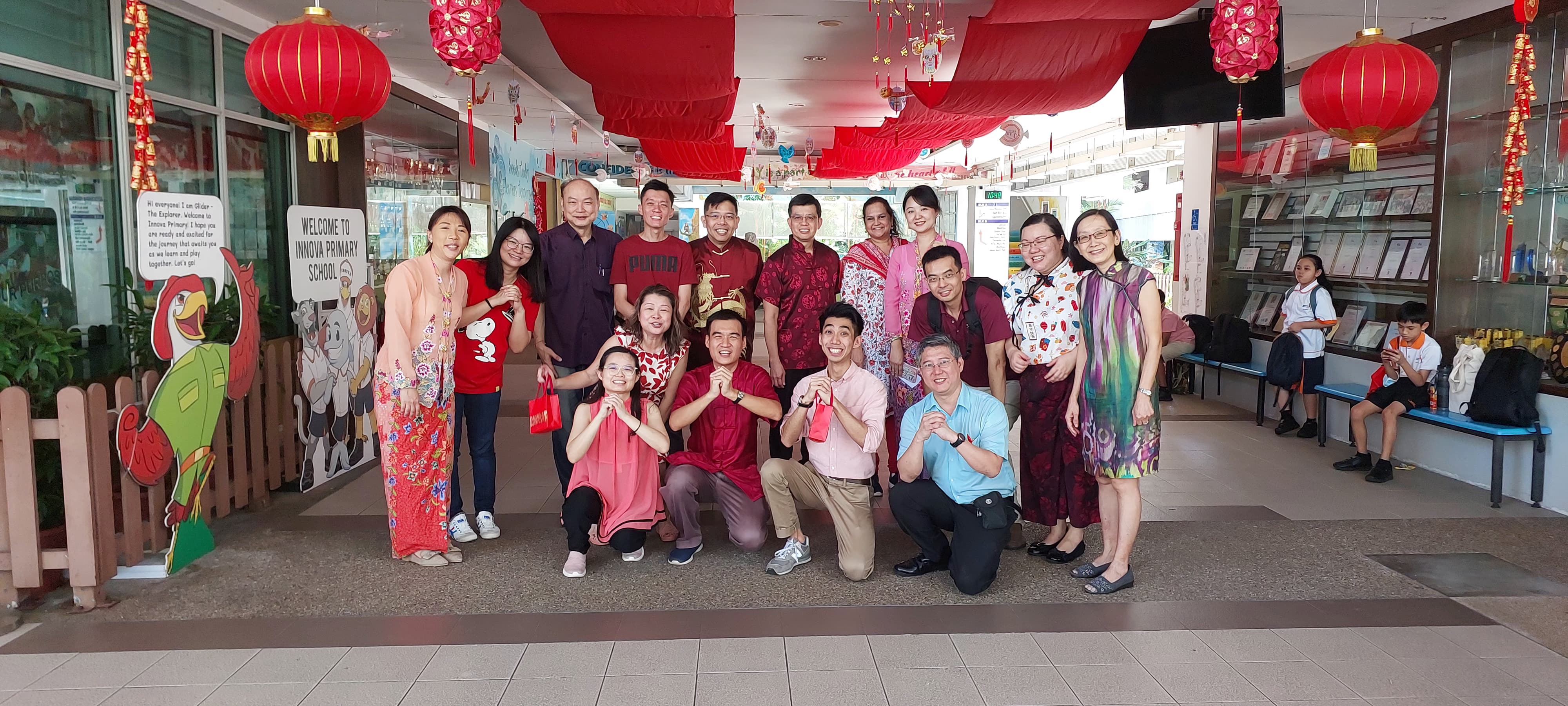 Group of adults posing at Innova Primary School entrance decorated with red Chinese New Year lanterns.