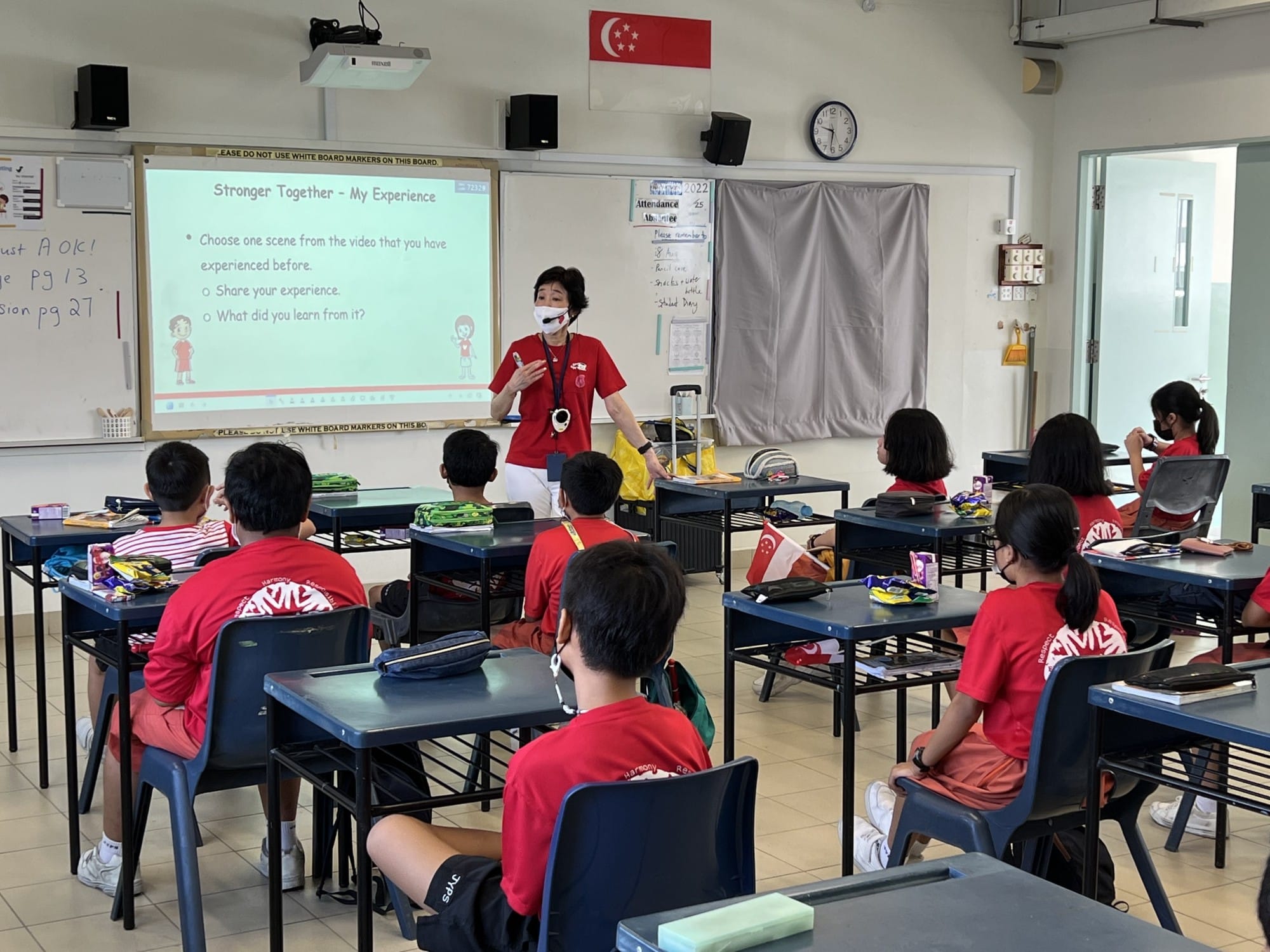 A masked teacher in red presents a slideshow titled "Stronger Together" to students in red uniforms in a Singapore classroom.