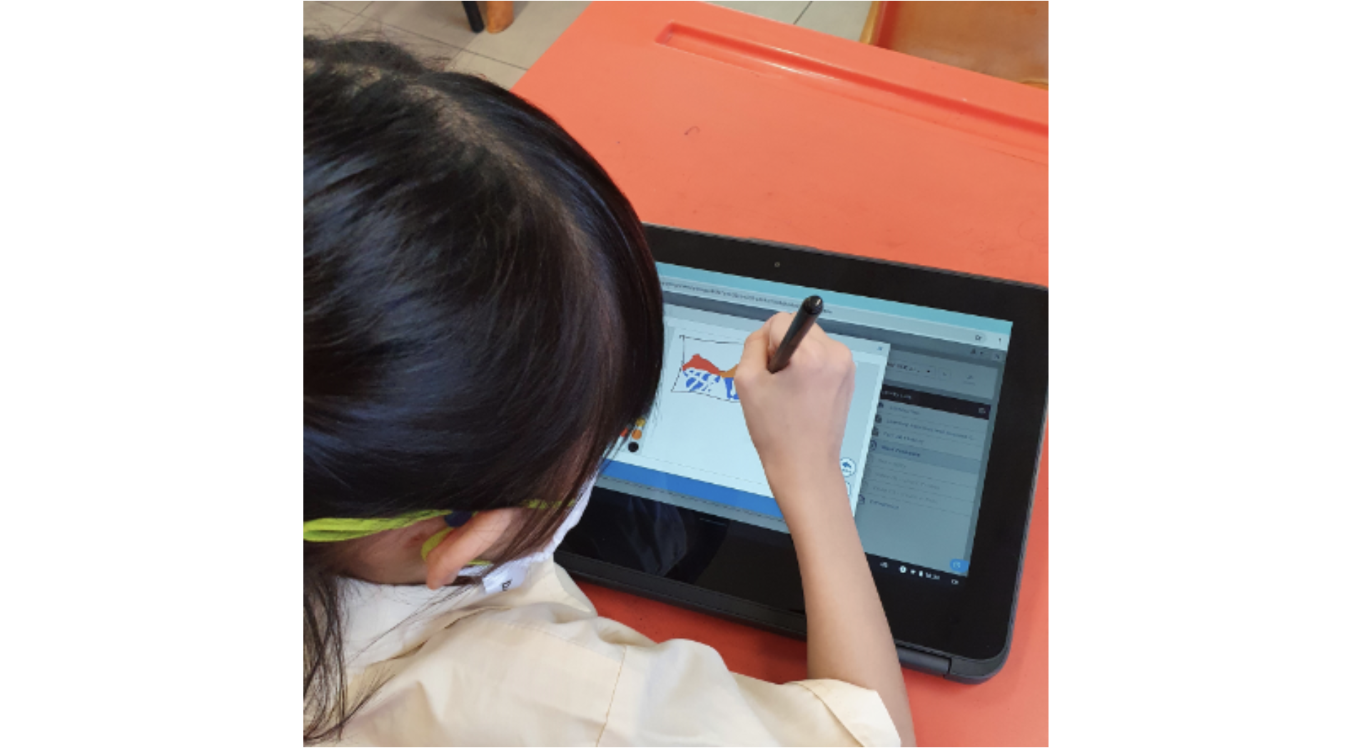 A young girl uses a stylus to draw on a touchscreen laptop placed on an orange desk.