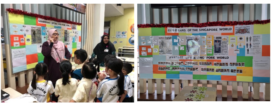 Two adults presenting a colorful "Guardians of the Singapore World" display board to young students in uniforms.