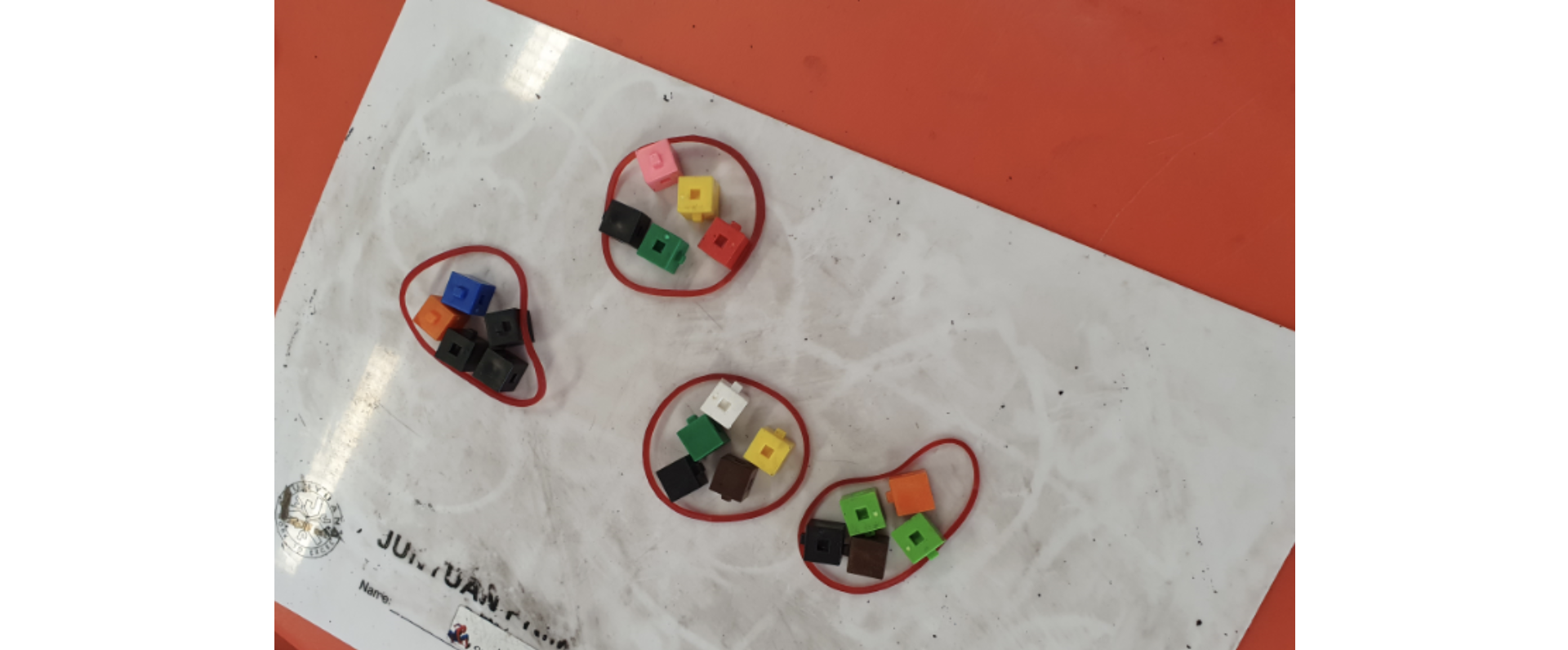 Four groups of colorful small plastic cubes separated by red rubber bands on a white paper sheet.