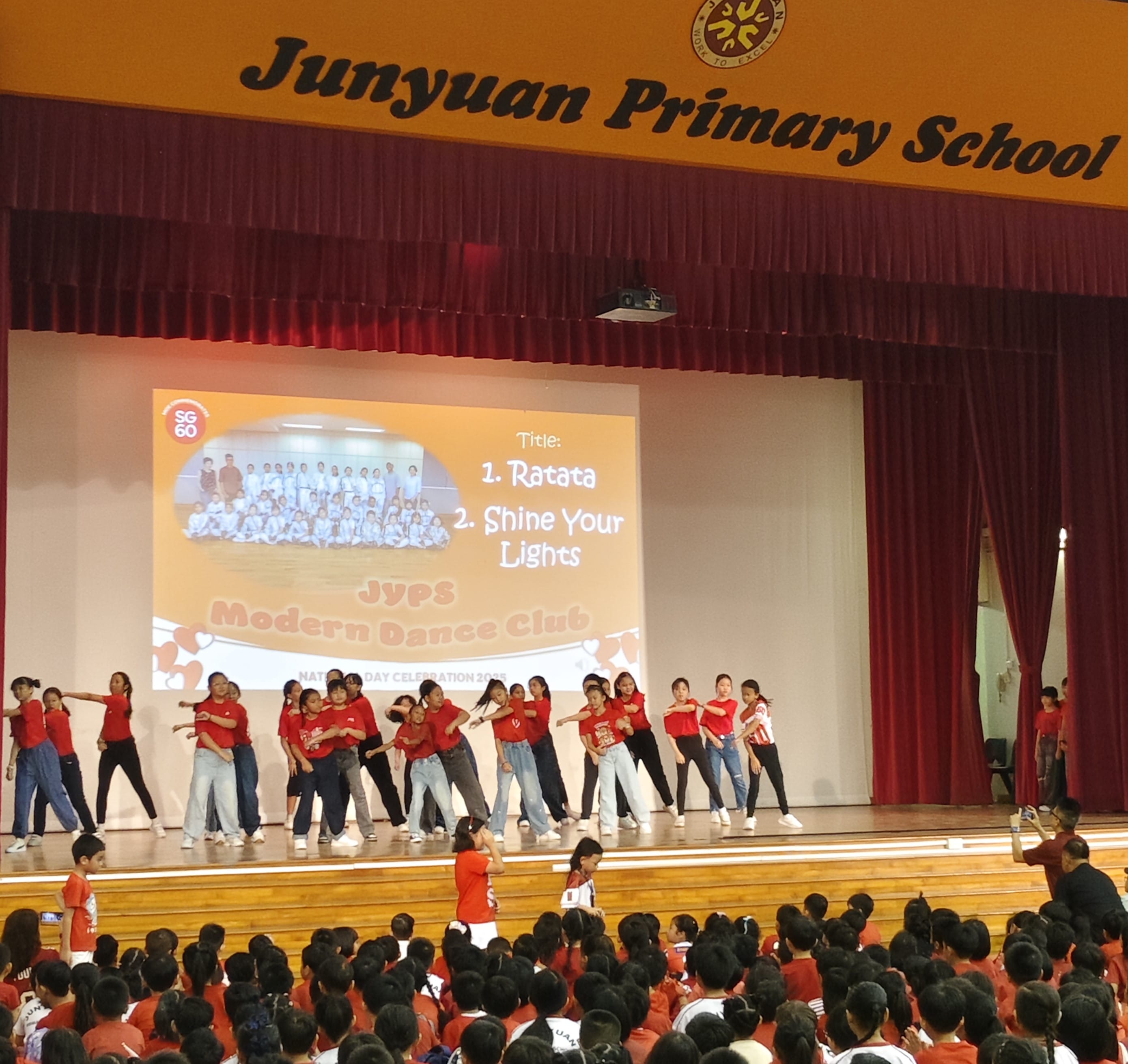 Students in red shirts perform a dance on stage at Junyuan Primary School's National Day Celebration.