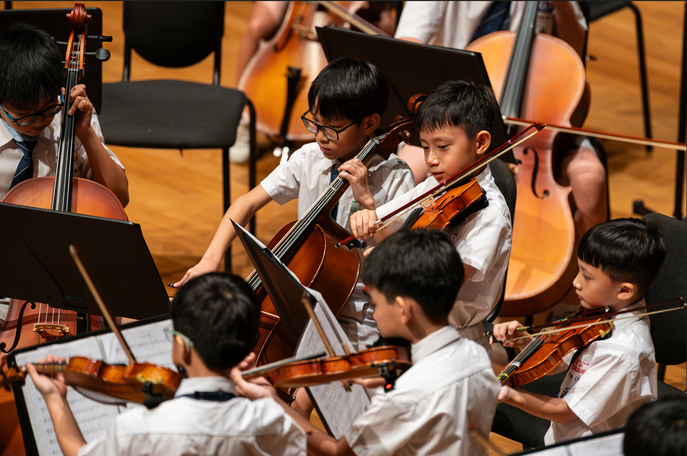 Five children from the string ensemble playing musical instruments during a practice.