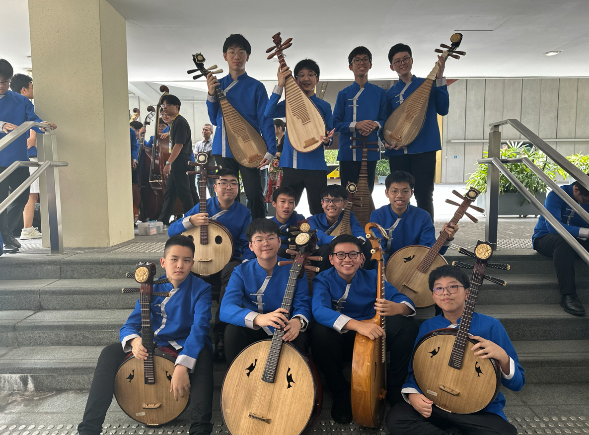 Three young musicians in blue uniforms playing erhu, a traditional Chinese two-stringed instrument, while seated.