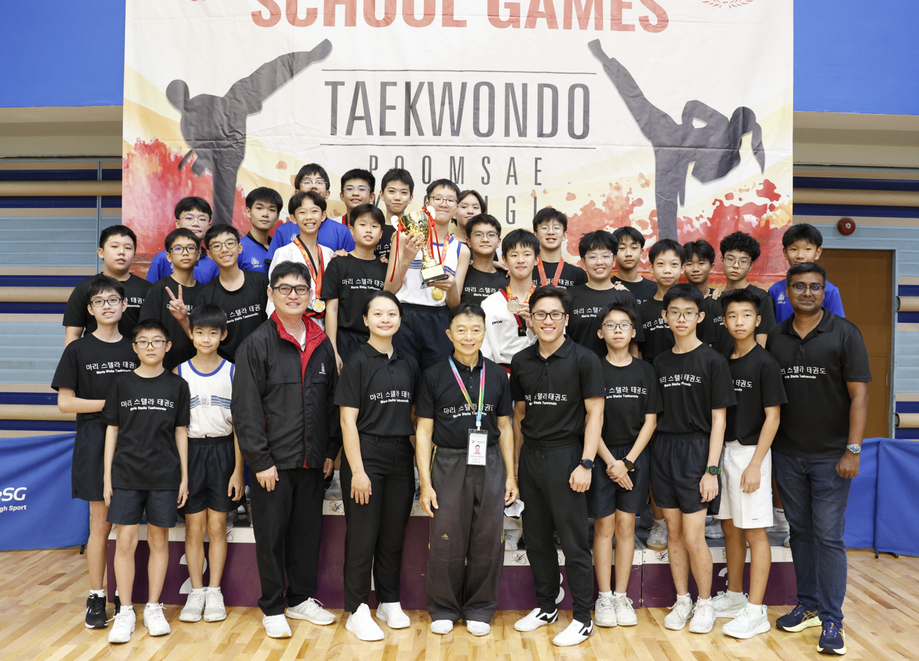 Students in white taekwondo uniforms and masks practice synchronized stances in a school gymnasium.