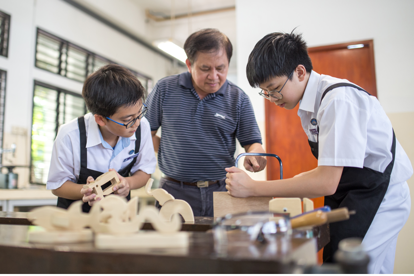Two male students in white shirts and aprons work together at a table during a hands-on activity.