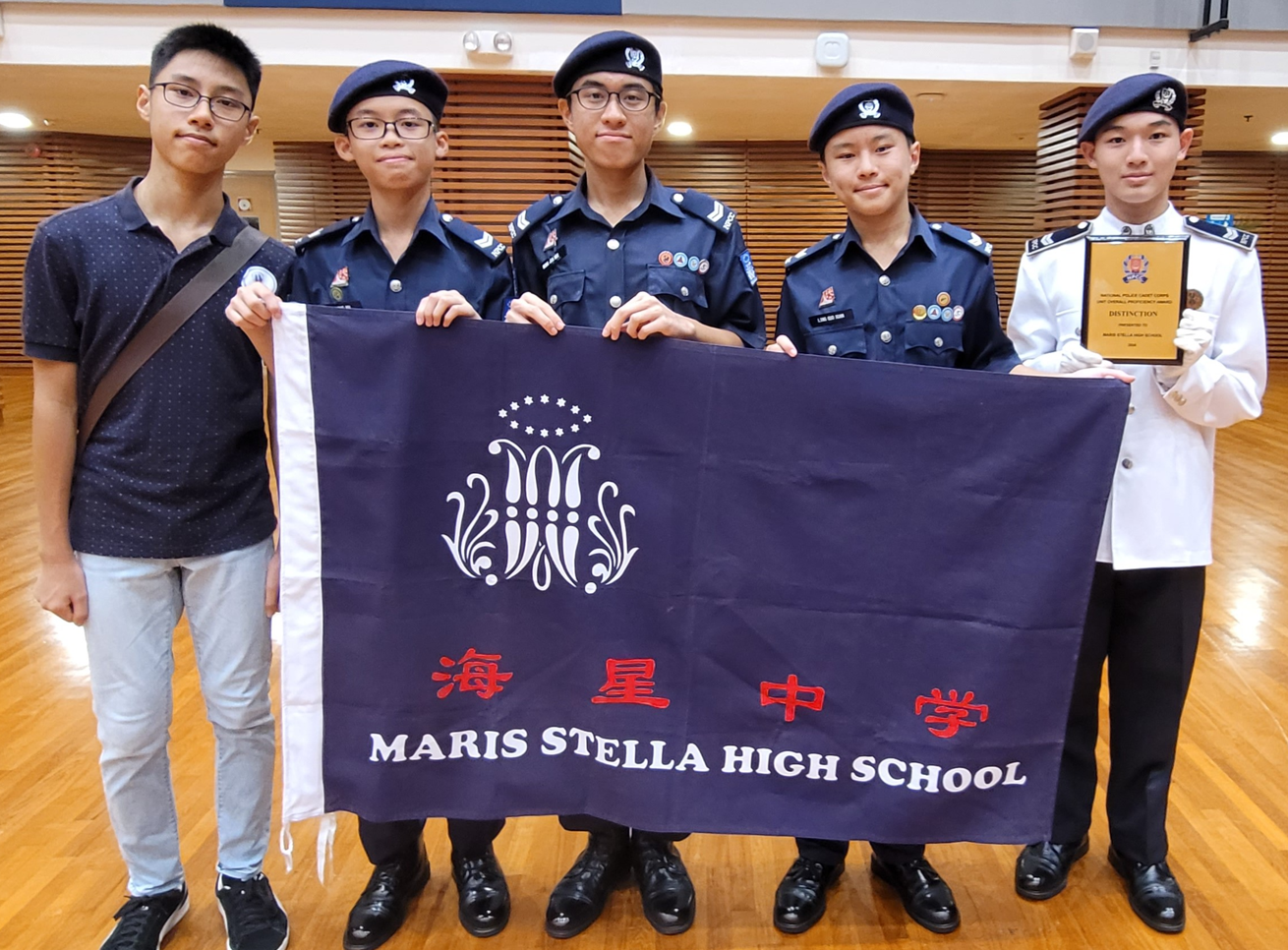 Young person in dark uniform and beret with glasses stands at attention before rows of similarly uniformed cadets.