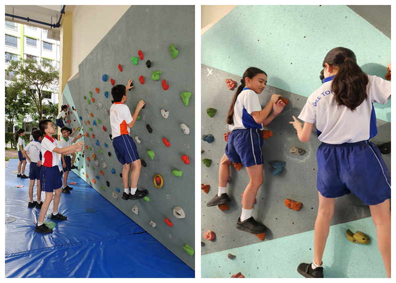 Students in school uniforms climbing and observing a colorful indoor rock climbing wall with multiple holds.