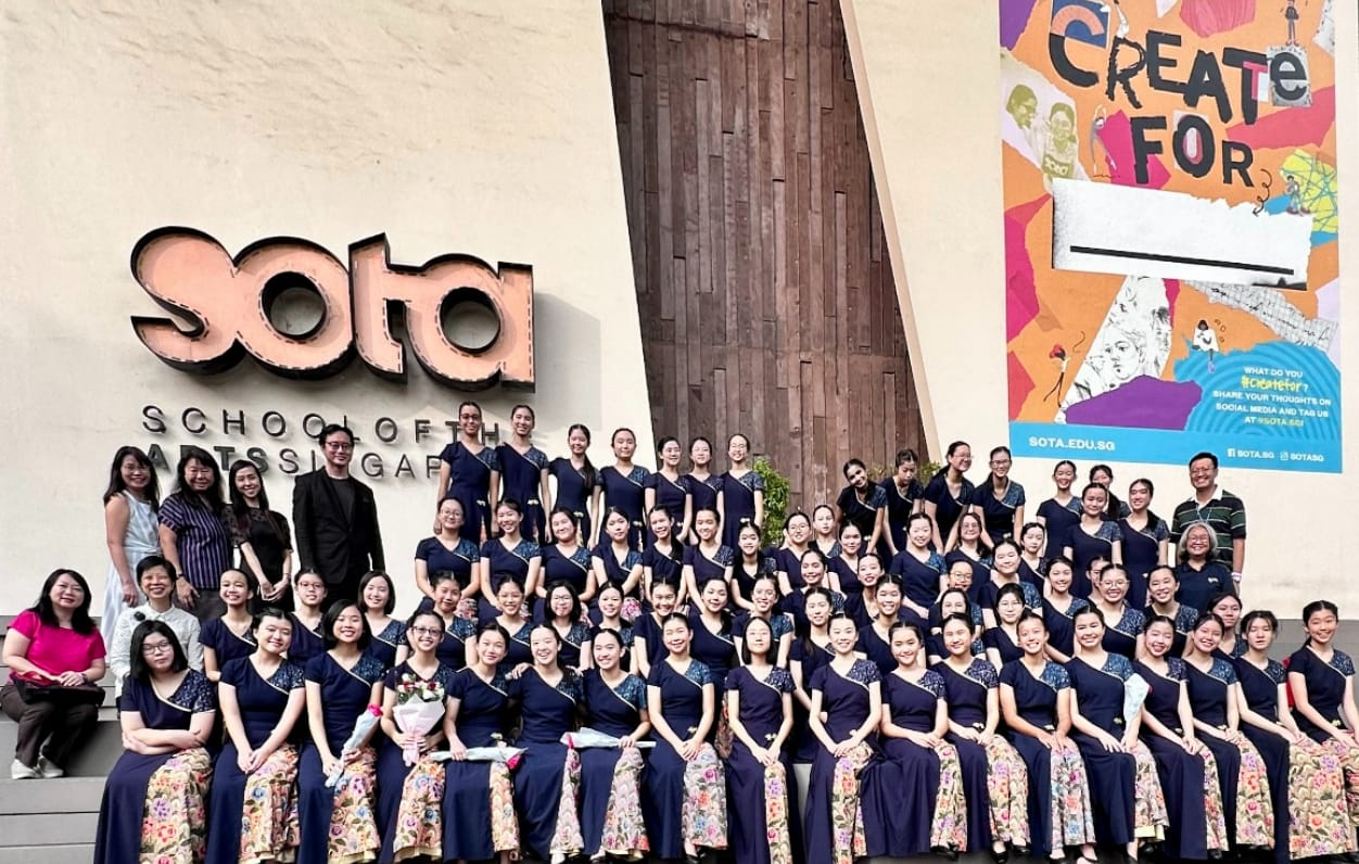 Large group of students in navy uniforms posing in front of the SOTA School of the Arts Singapore building.
