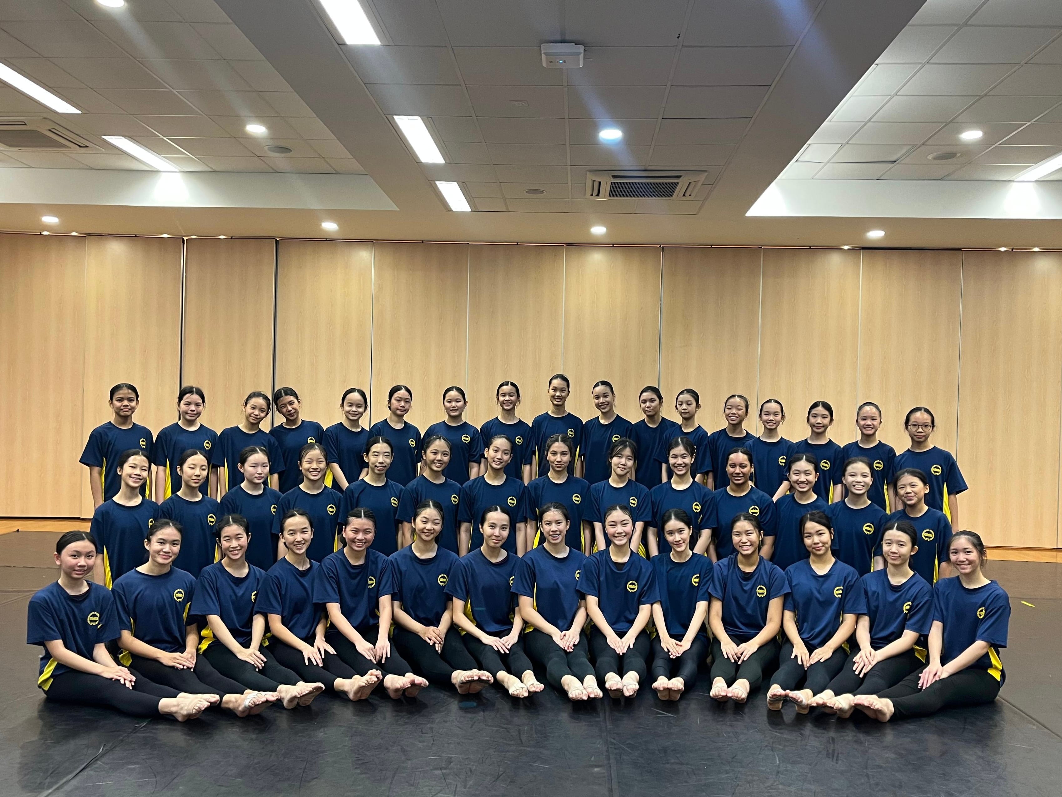 Large group of young female dancers in navy blue uniforms posing together in an indoor dance studio.
