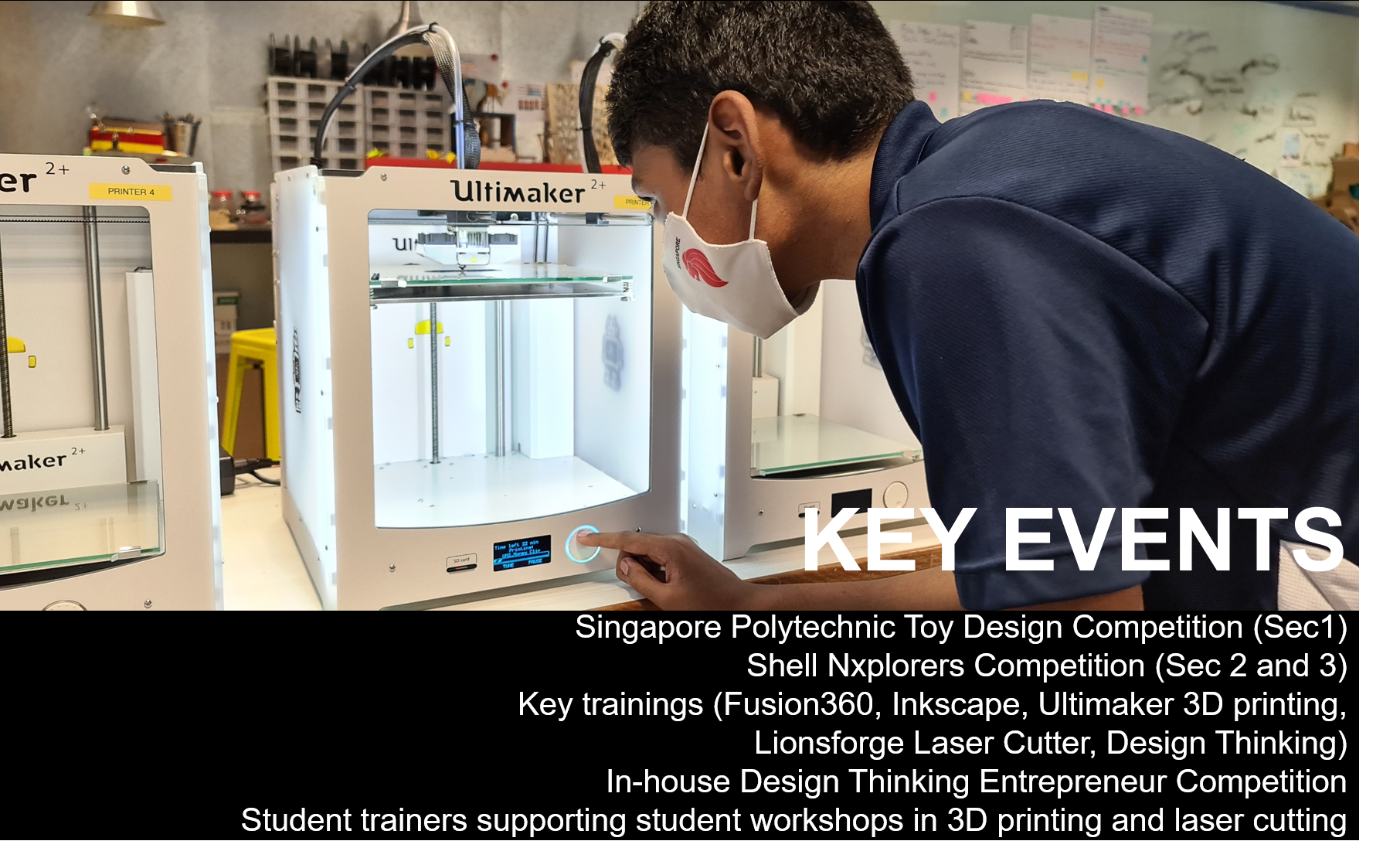 A masked student leans over an Ultimaker 2+ 3D printer, pressing its control button in a lab.