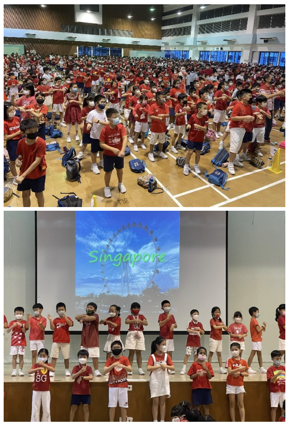 Children in red outfits and masks perform a group activity in a hall and on a stage with a Singapore projection.