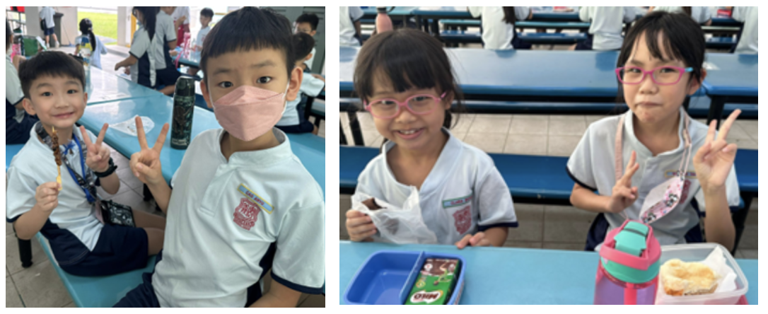 Four young students in school uniforms sit at blue canteen tables, smiling and making peace signs.