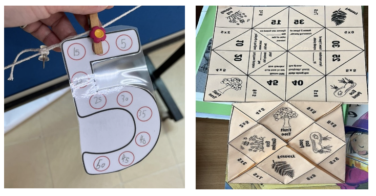 A number 5 cutout with multiples of 5 written in circles, beside paper fortune tellers with multiplication facts.