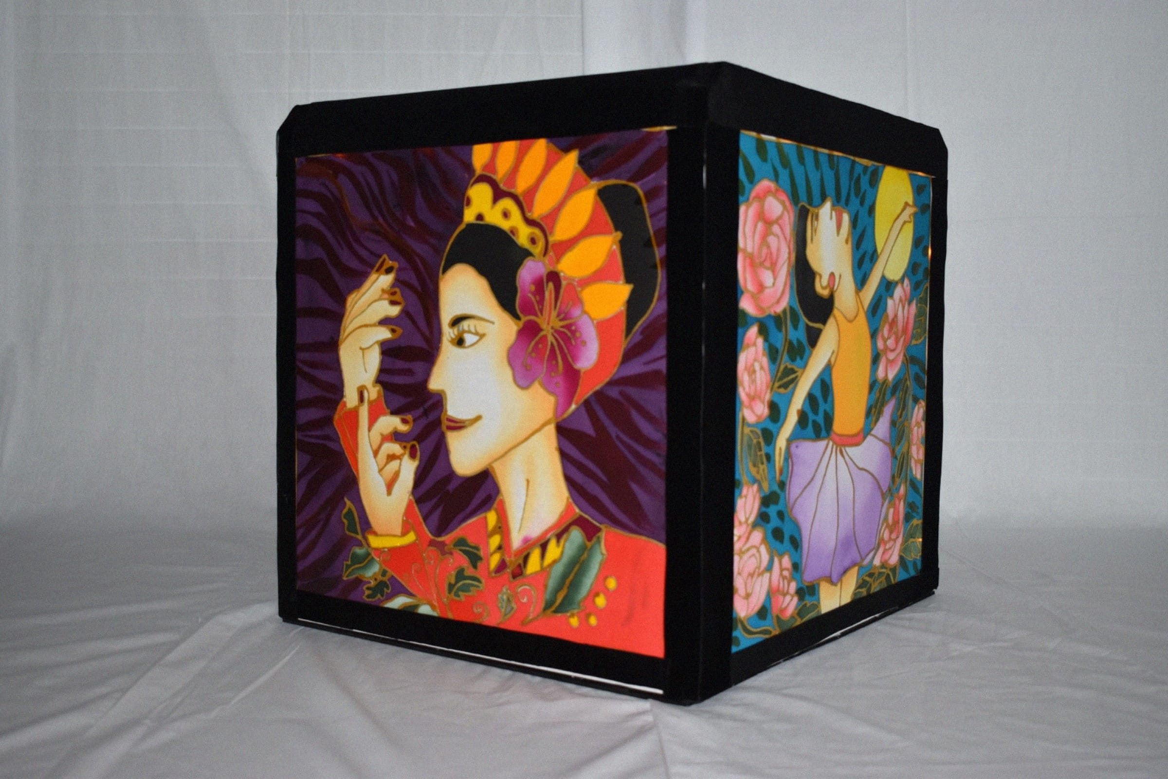 Black cube lamp with colorful art panels showing a woman in a decorative headdress and a ballerina among pink roses.