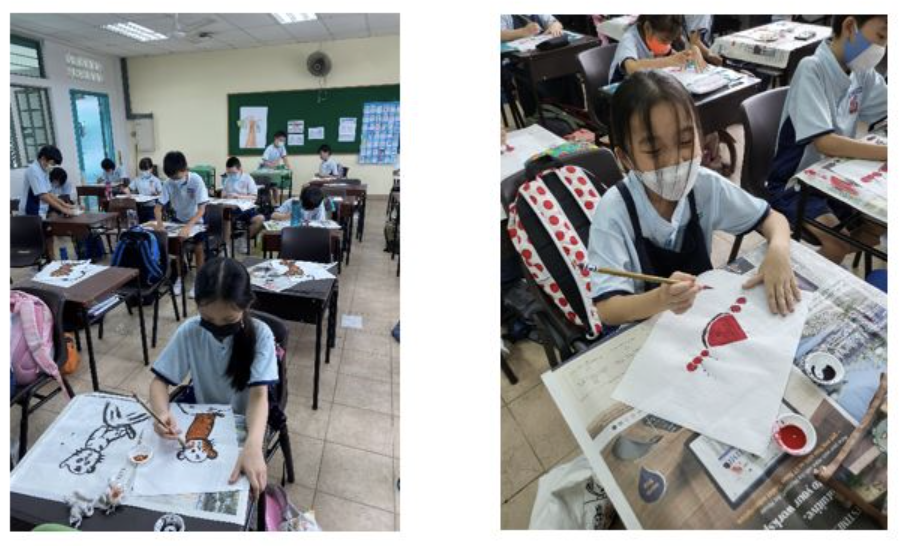 Students wearing masks paint artwork at school desks in a classroom art activity.