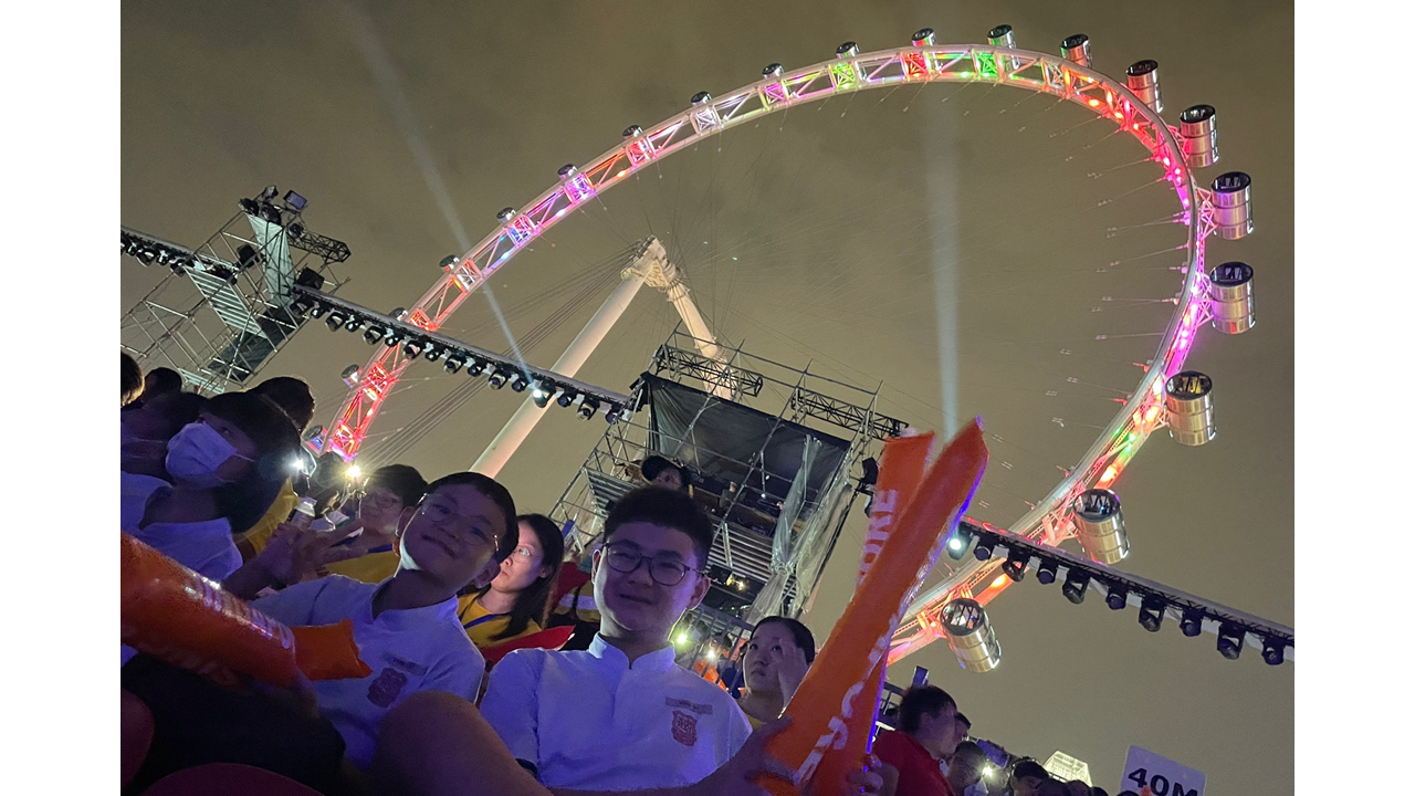 A crowd of people at a nighttime outdoor event with a large colorful lit Ferris wheel in the background.