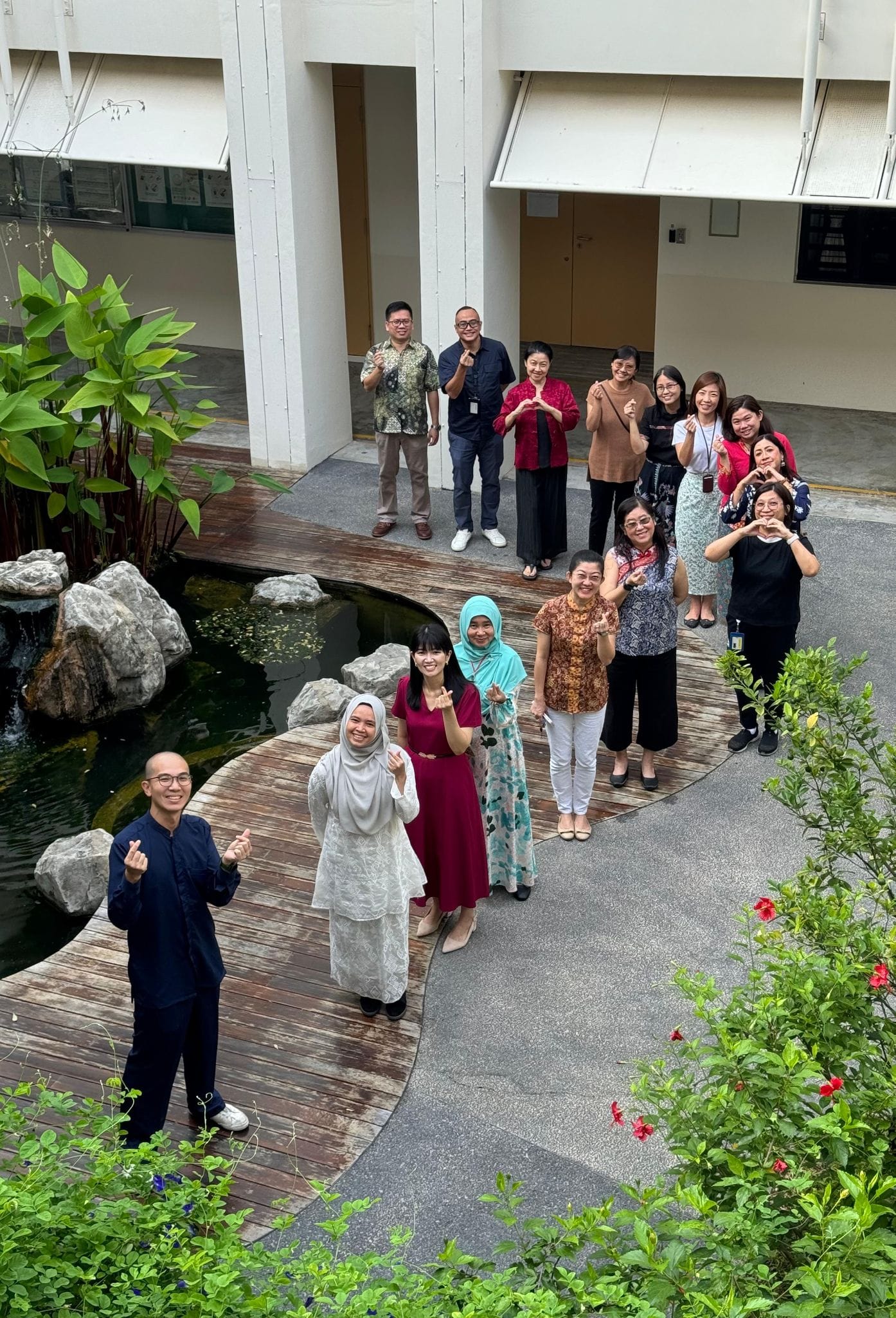A group of school staff posing in front of a pond, while making heart hand gestures.