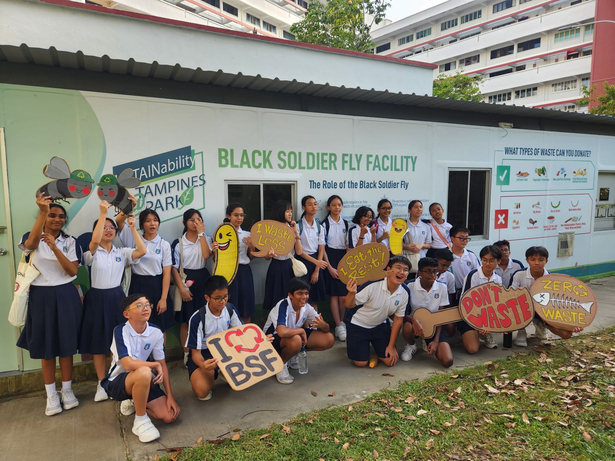 Ngee Ann Secondary students posing with zero waste signs in front of a Black Soldier Fly Facility.