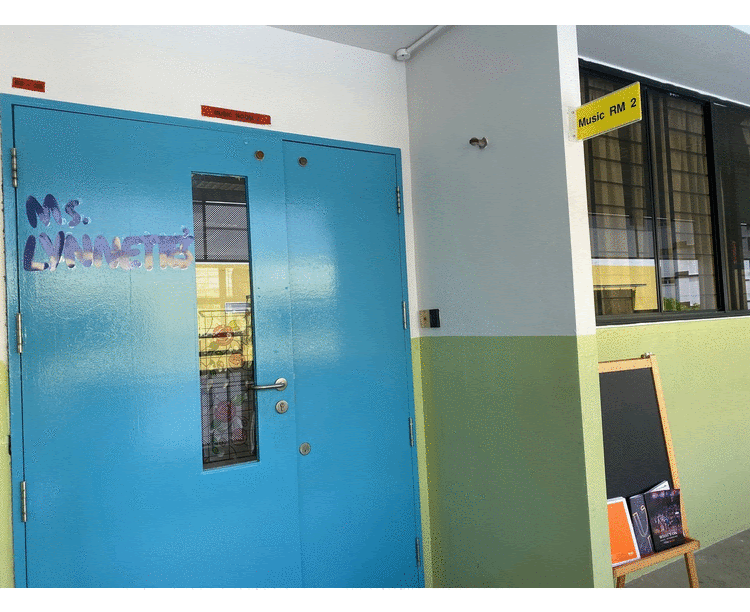 A blue classroom door labeled Ms. Lynnette's with a yellow sign reading Music RM 2 on the wall beside it.