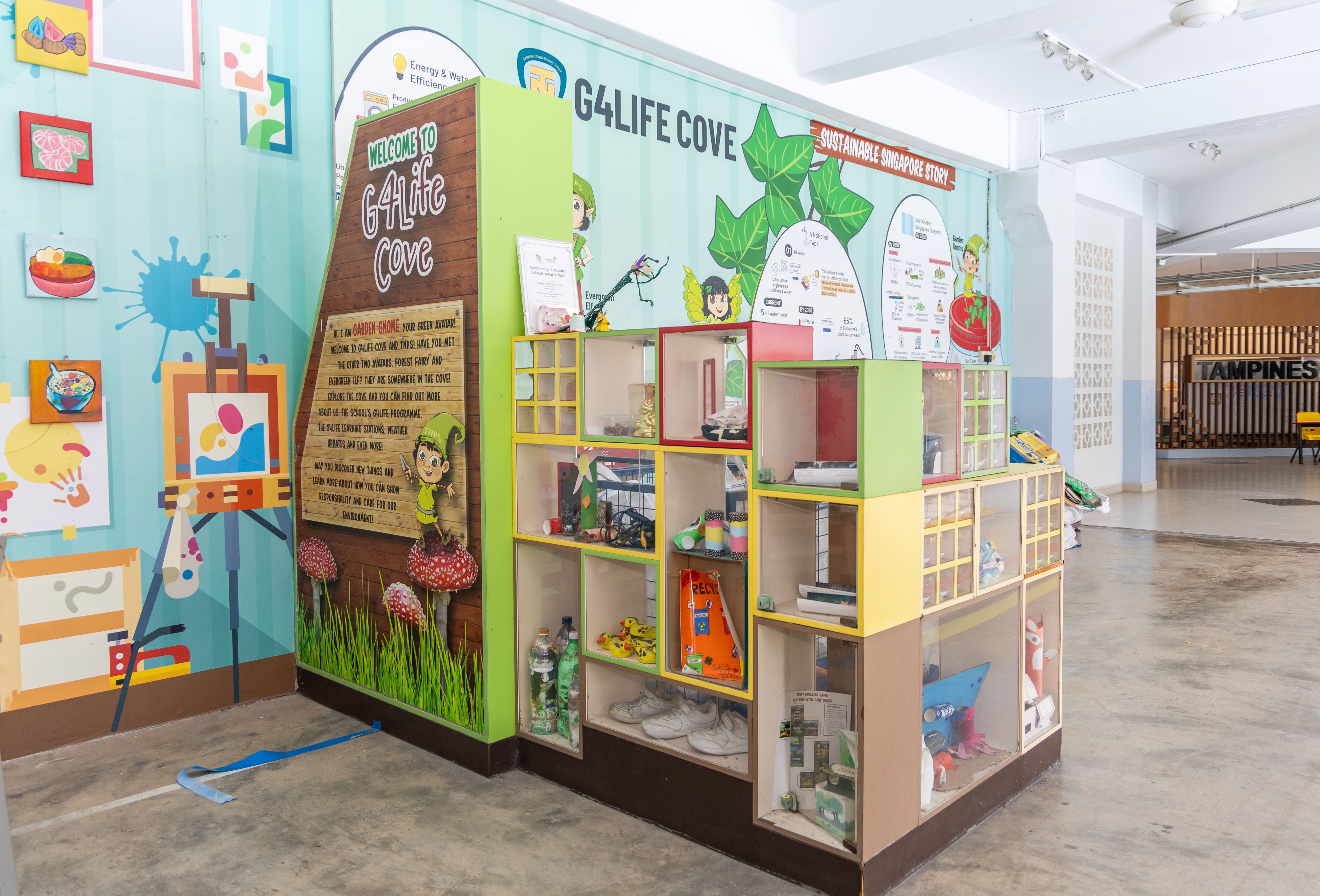 Colorful G4Life Cove educational display with shelves holding recycled items, cartoon characters, and sustainability-themed signage.