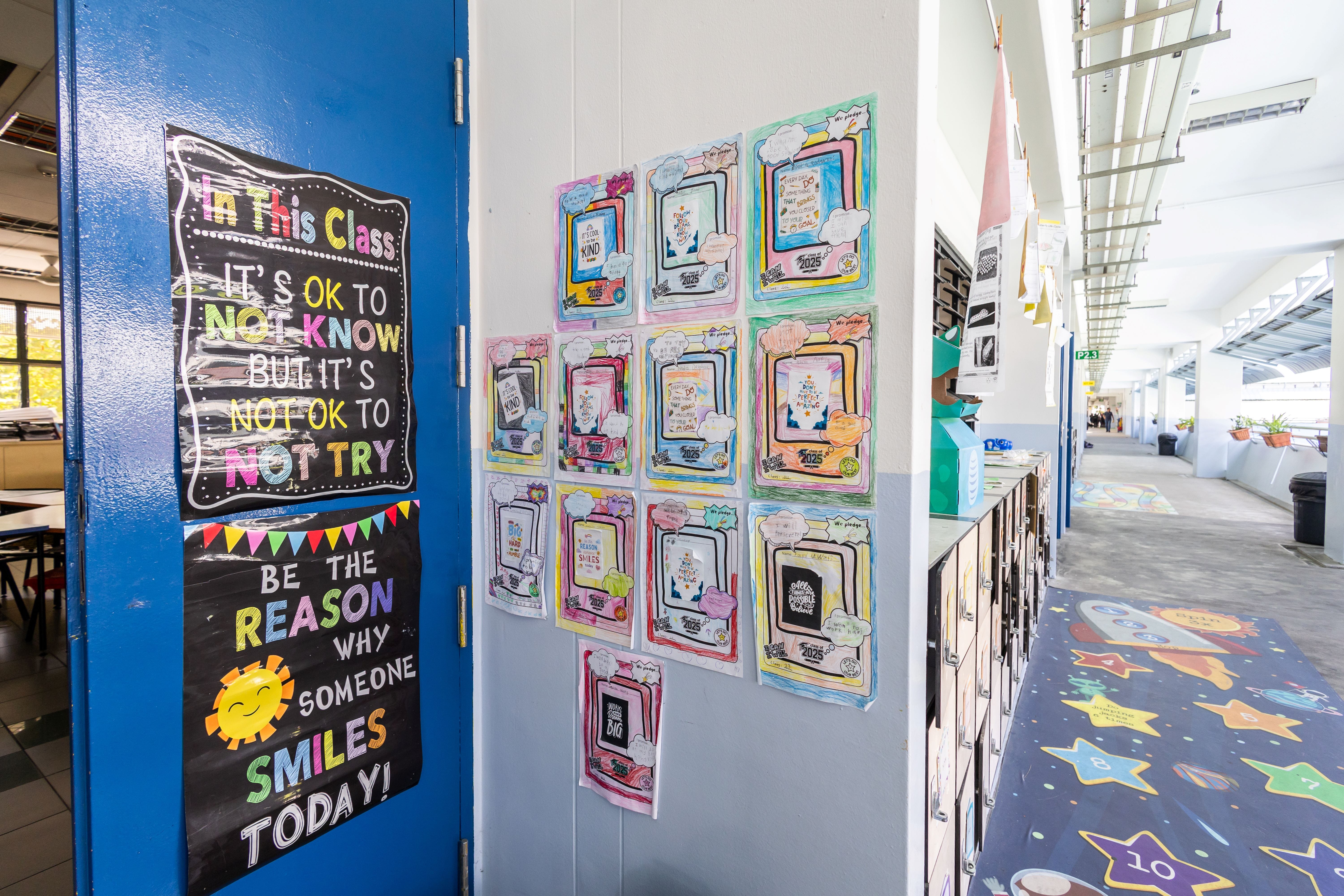 Colorful motivational posters on a blue classroom door and student artwork displayed on a white wall in a school corridor.