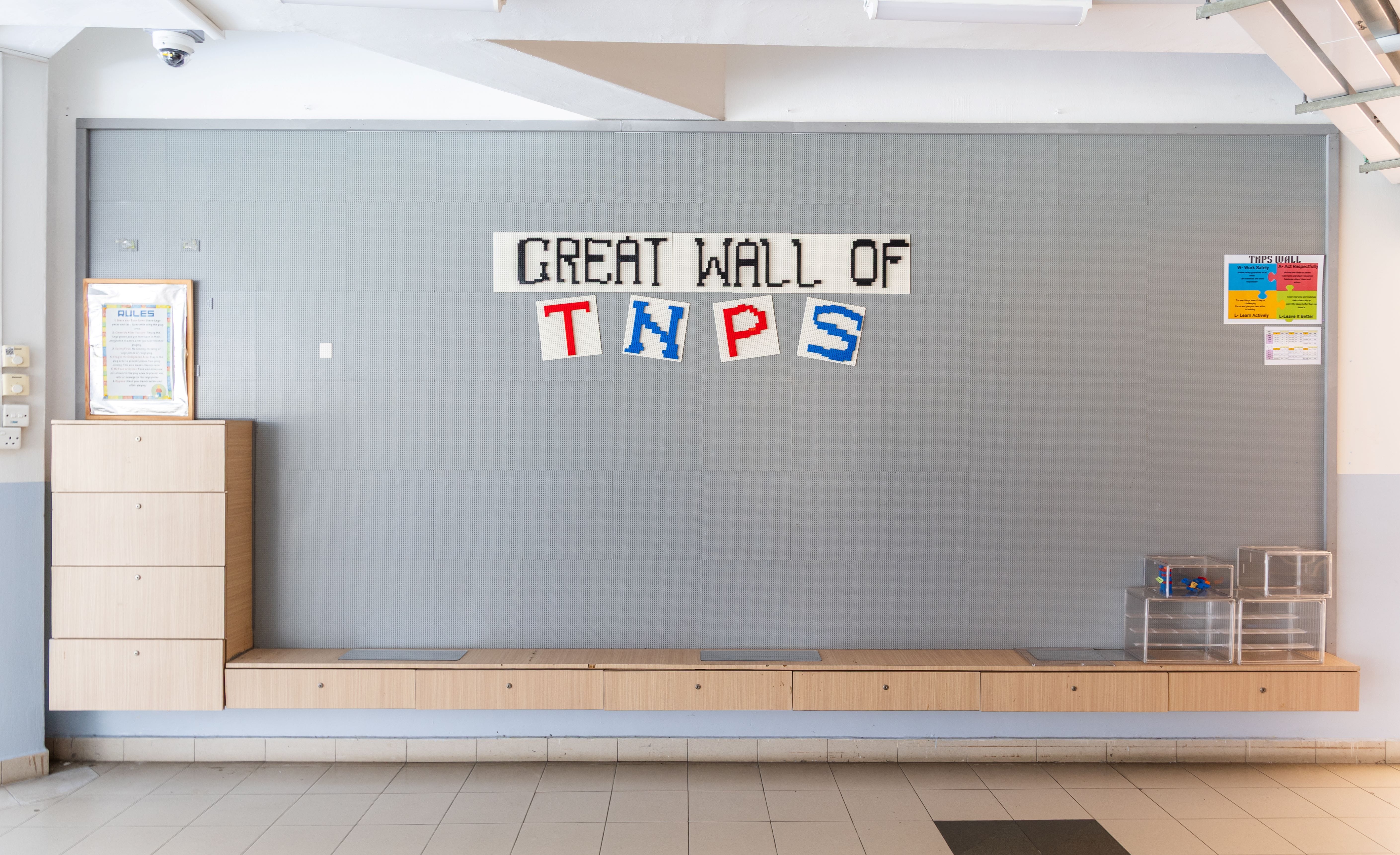 A gray LEGO board wall displaying "Great Wall of TNPS" in colorful brick letters inside a school corridor.
