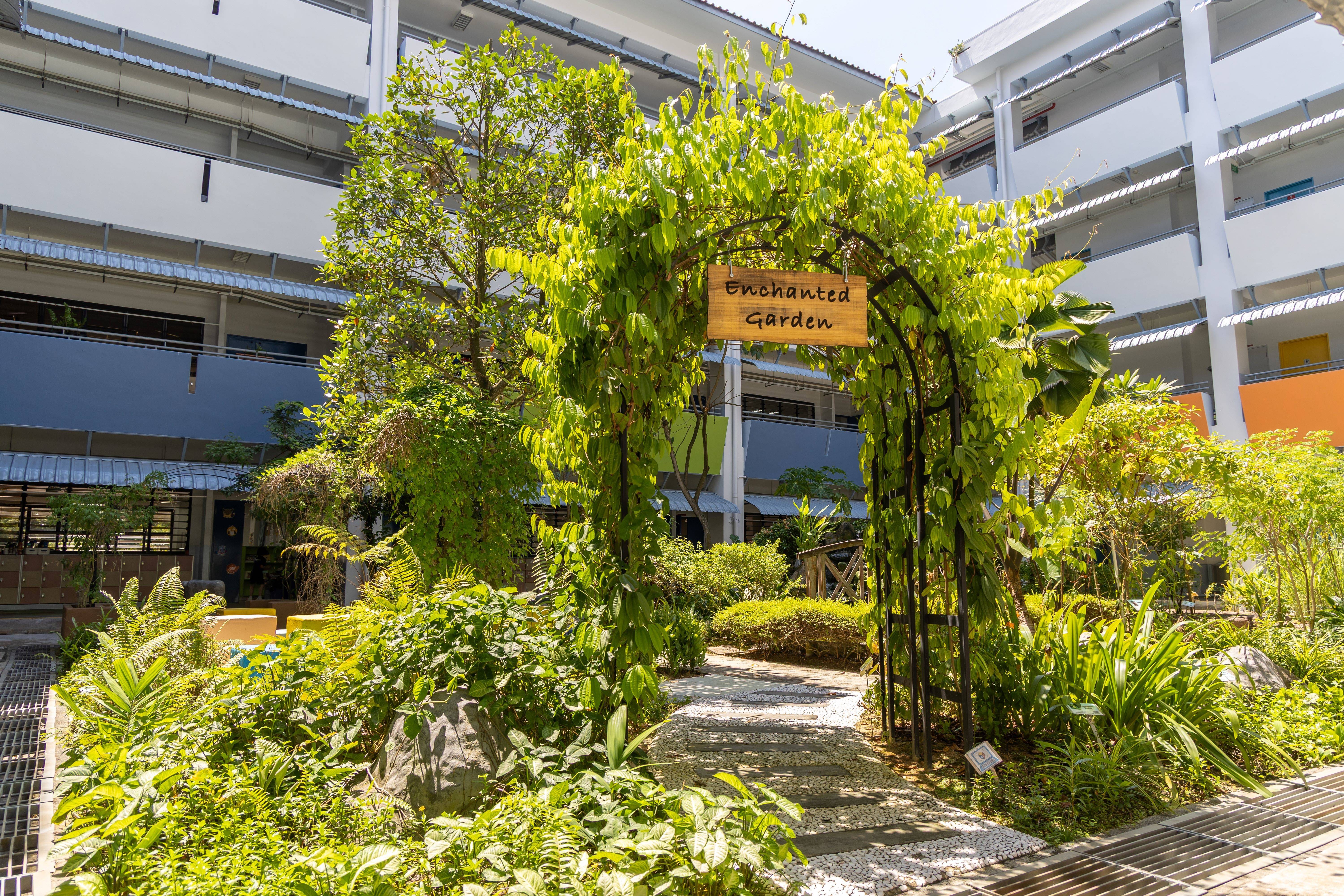 Leafy vine arch with a wooden Enchanted Garden sign over a stone path in a courtyard garden.