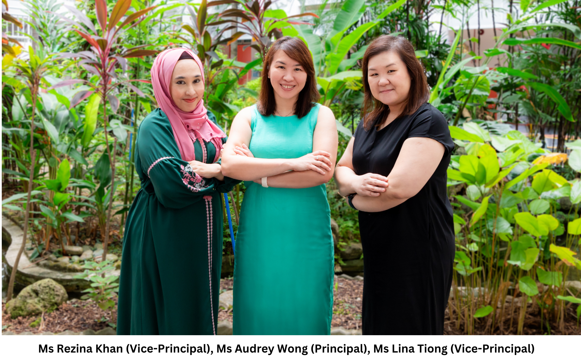 Three women pose with arms crossed in a garden; one wears a pink hijab, others wear teal and black dresses.
