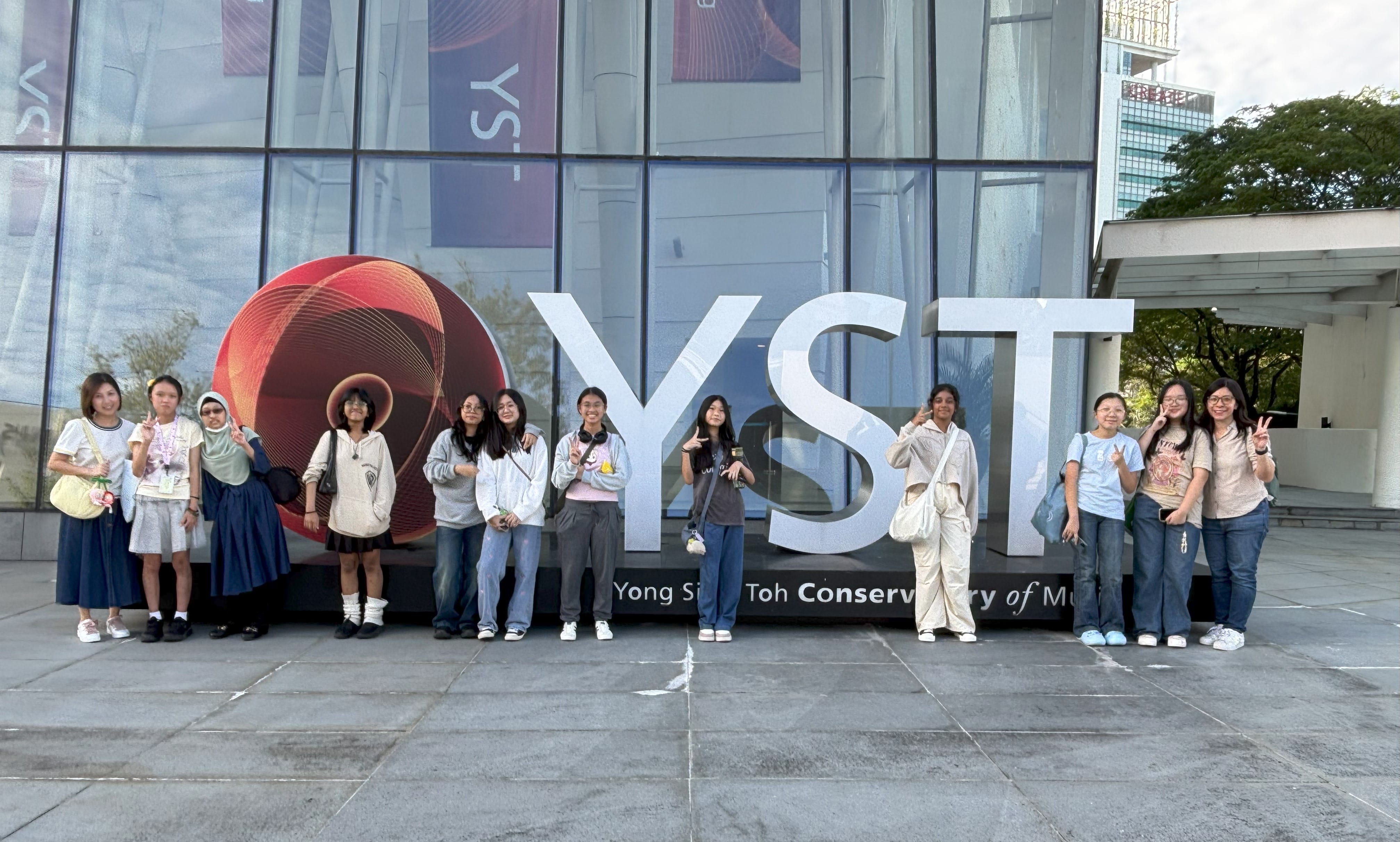 A group of young people posing in front of the large YST Yong Siew Toh Conservatory of Music sign.