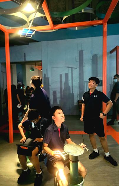 Students in uniforms explore an interactive science museum exhibit with colorful metal frames and glowing displays.