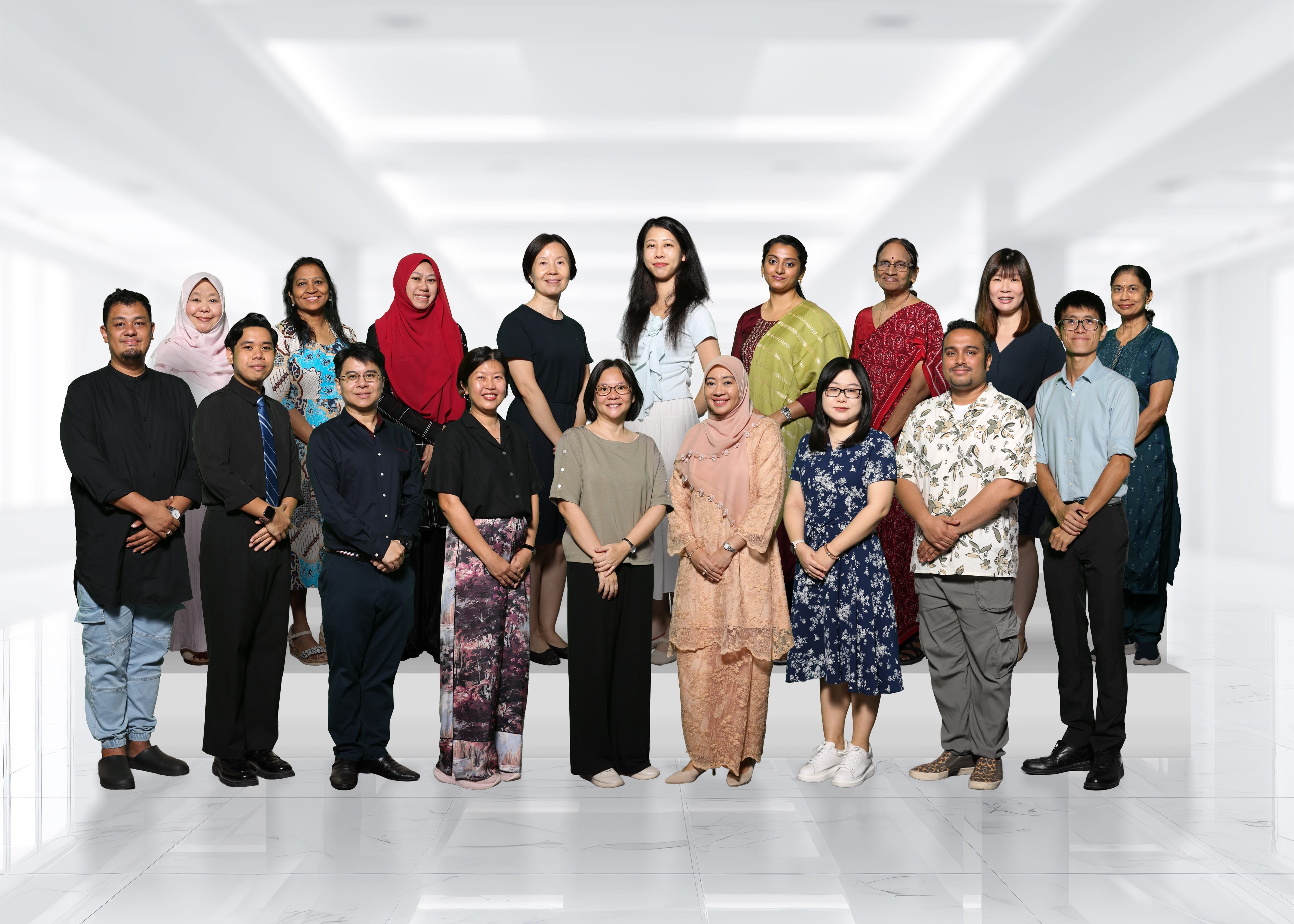 A diverse group of about 18 adults posing together in two rows in a bright white indoor hallway.