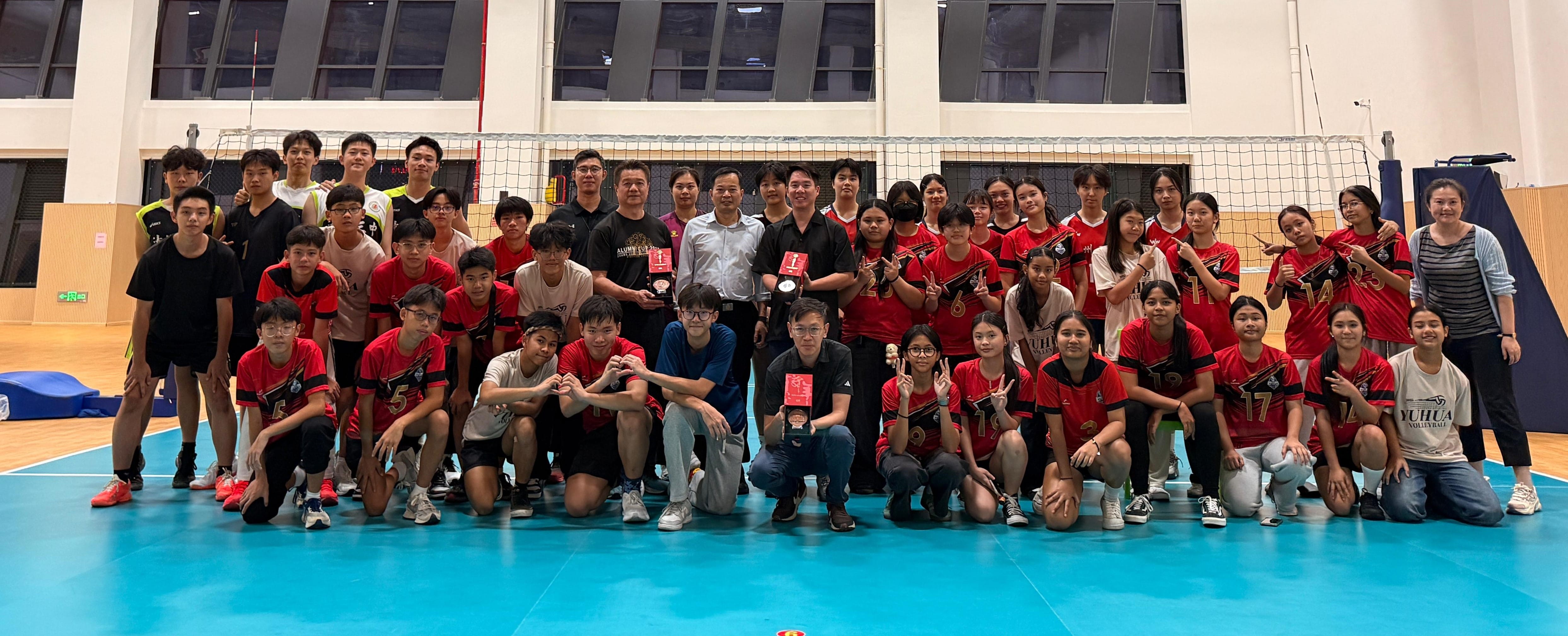 Large group of volleyball players in red uniforms posing together on an indoor court in front of a net.