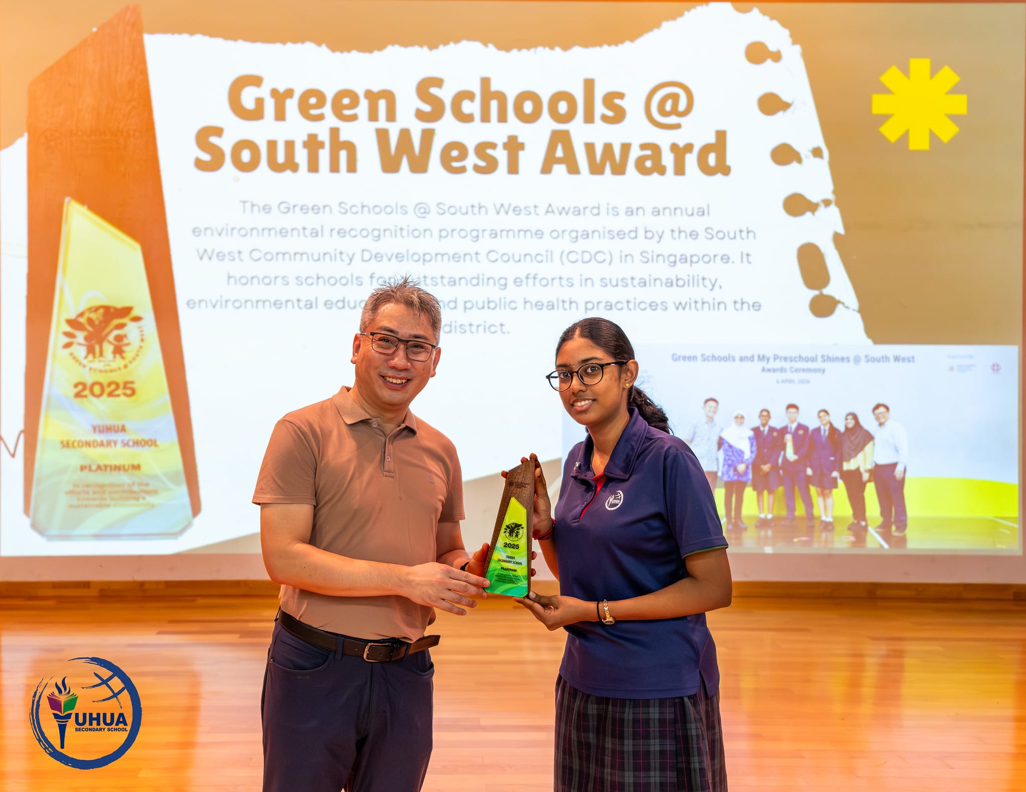 Two people hold a trophy together in front of a Green Schools at South West Award 2025 presentation slide.